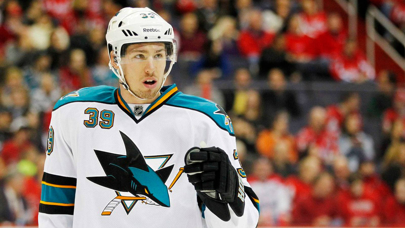 hockey 桌布 壁紙 — 一名專注的冰球運動員身穿白色聖荷西鯊魚隊39號球衣，在比賽中站在冰上，背景是模糊的人群。