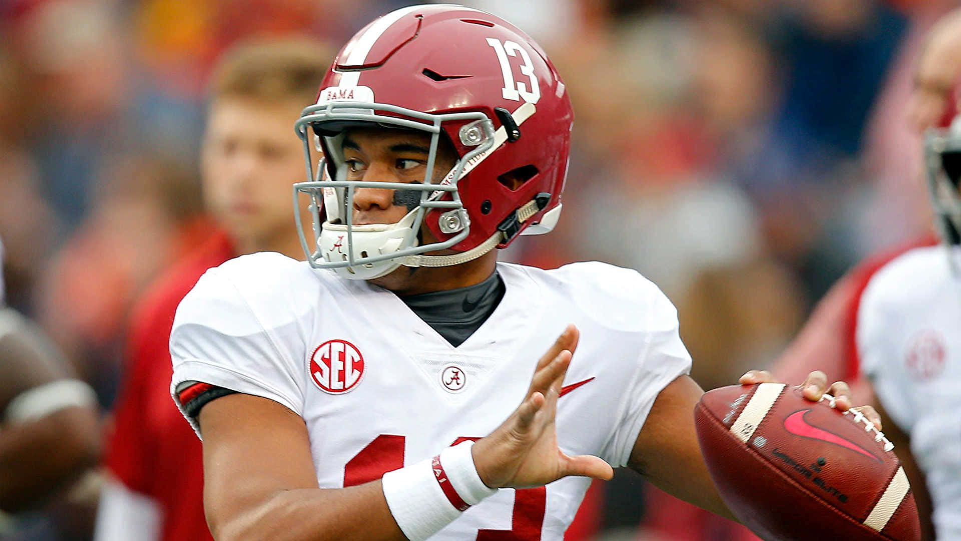 Tua Tagovailoa 桌布 壁紙 — 一名專注的大學美式足球四分衛，戴著深紅色頭盔，穿著白色球衣，在日間比賽中準備傳球。