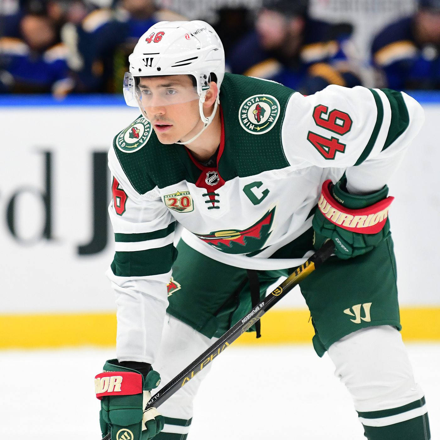 hockey 桌布 壁紙 — 一名專注的明尼蘇達荒野冰球球員，身穿綠色和白色裝備，在冰上蹲下，比賽期間握著球桿。