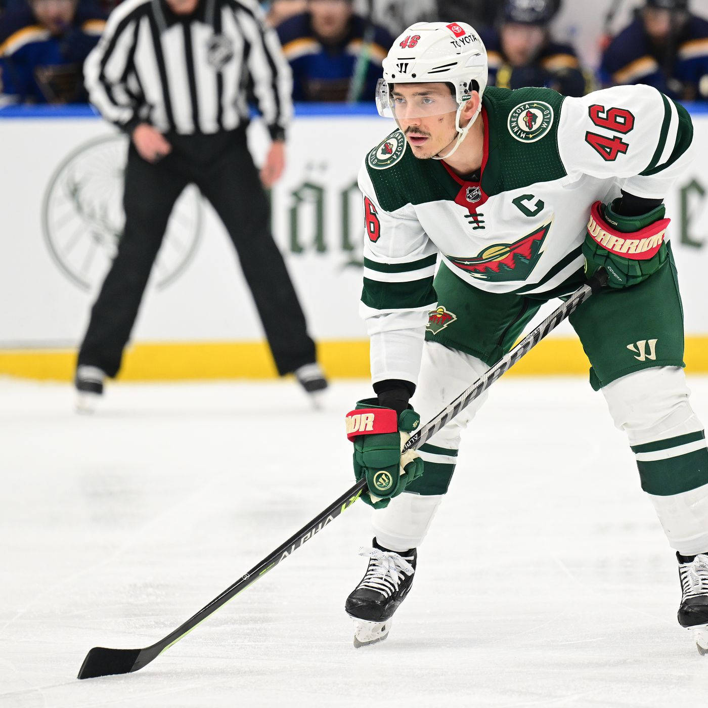 hockey 桌布 壁紙 — 一名專注的曲棍球運動員穿著綠色和白色的裝備，在冰上激烈滑行，背景有裁判。