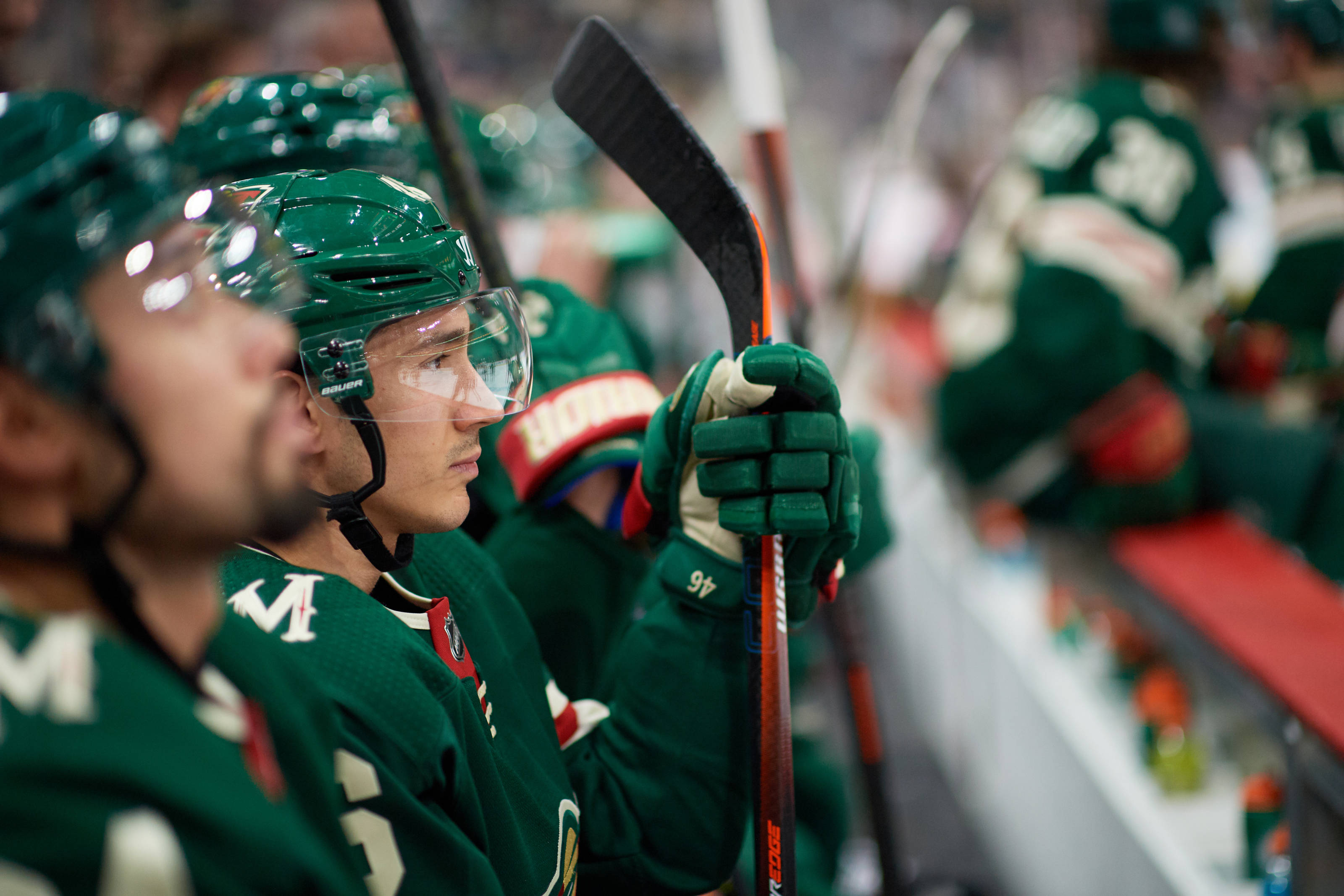 hockey 桌布 壁紙 — 一名專注的曲棍球運動員穿著綠色裝備，在比賽期間坐在長凳上握著球棍。