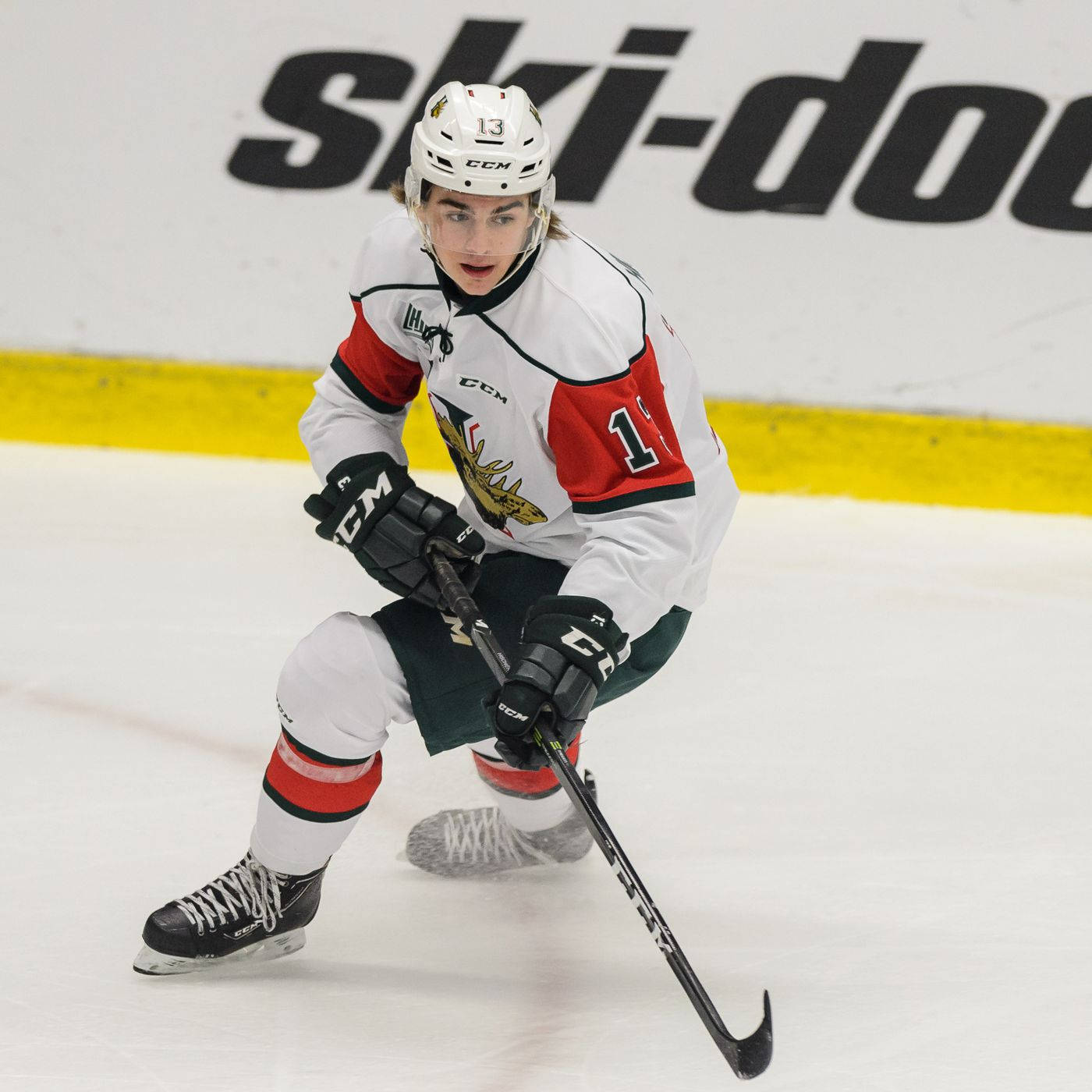 hockey 桌布 壁紙 — 一名專注的曲棍球運動員身穿白、紅、綠色制服，在比賽中持棍在冰上激烈滑行。