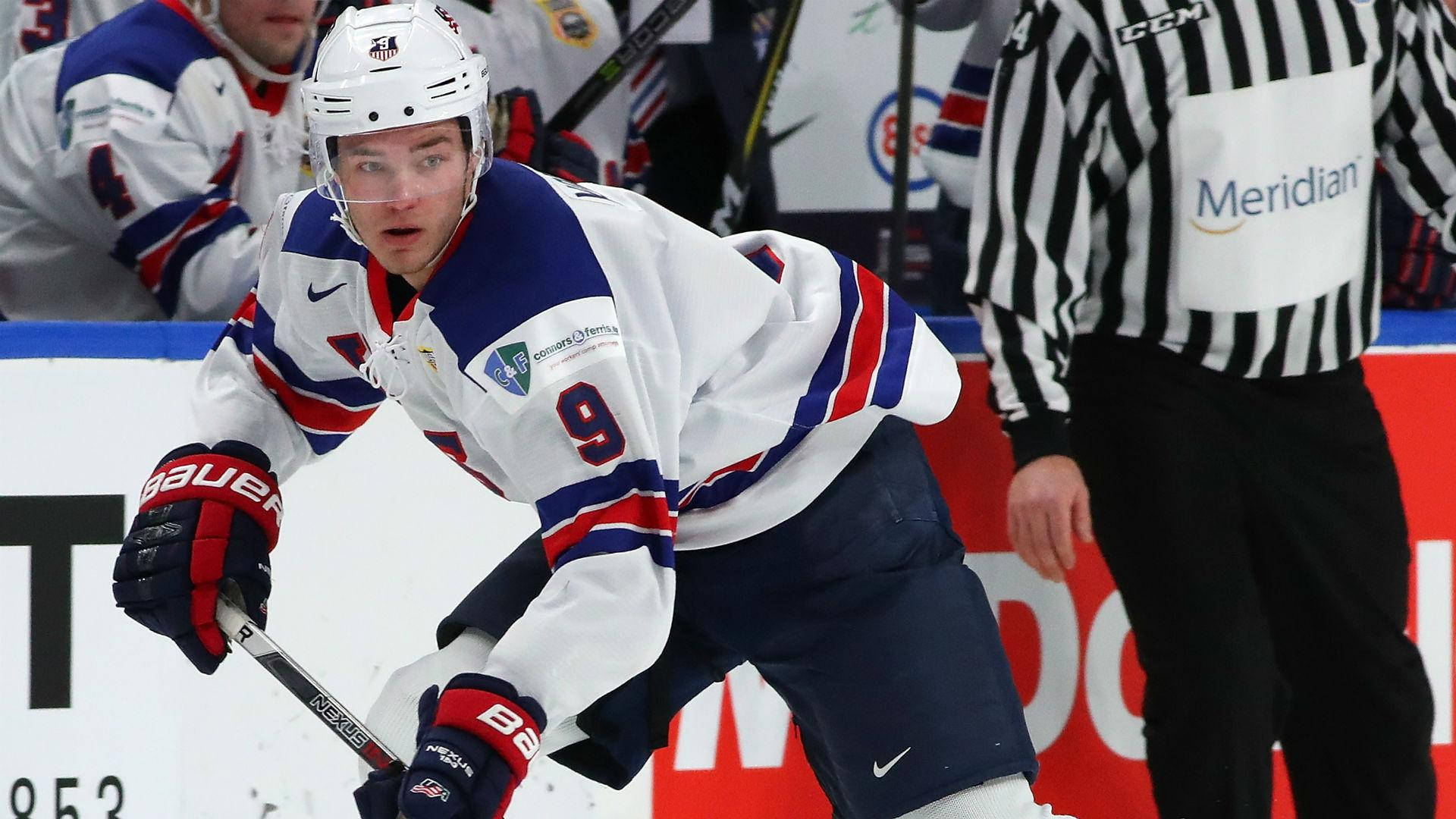 hockey 桌布 壁紙 — 一名專注的曲棍球運動員身穿白、藍、紅色球衣，在冰上激烈滑行，附近有裁判。