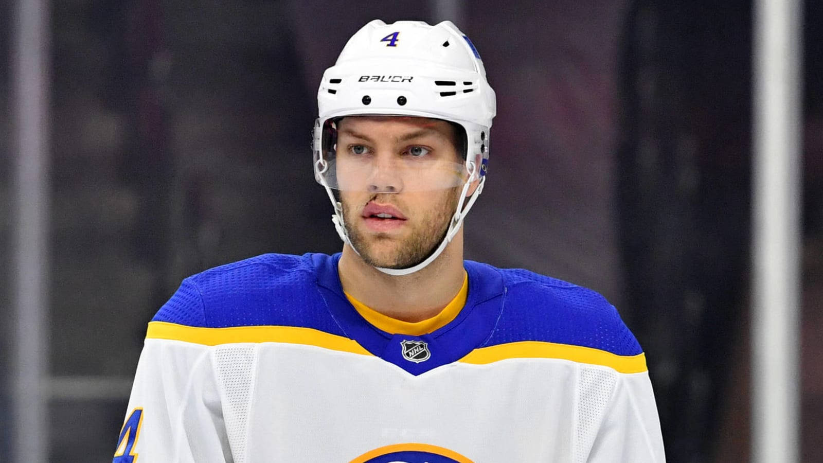 hockey 桌布 壁紙 — 一名專注的曲棍球運動員身穿白色、藍色和黃色球衣，背號四號，在比賽中凝視前方。