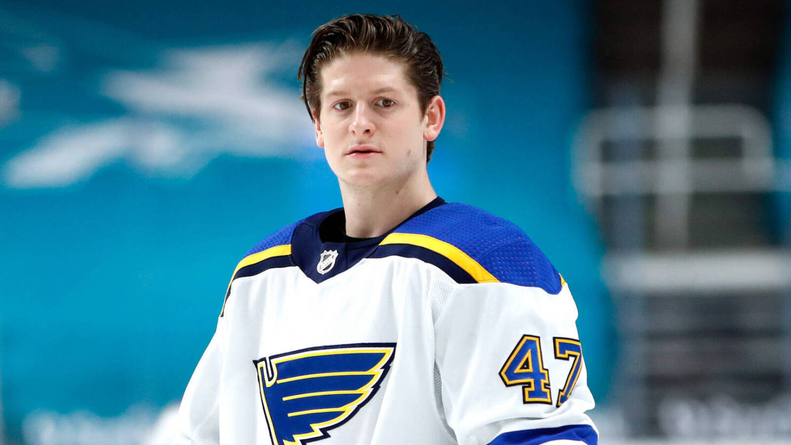 St Louis Blues 桌布 壁紙 — 一名專注的曲棍球運動員身穿白色、藍色和金色的47號球衣，站在冰面上，背景是模糊的競技場。