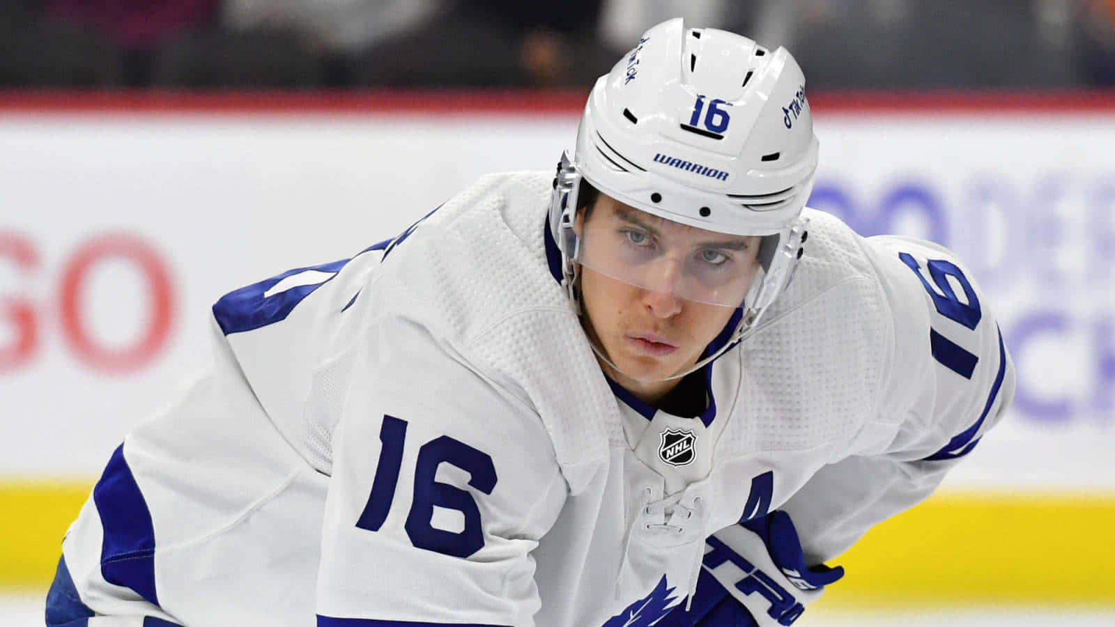 hockey 桌布 壁紙 — 一名專注的曲棍球運動員身穿白色和藍色裝備，背號16，在冰場上比賽時身體前傾。