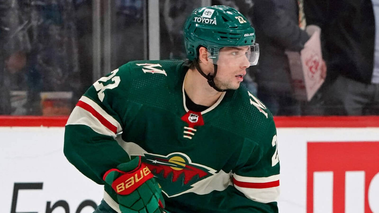 hockey 桌布 壁紙 — 一名專注的曲棍球運動員身穿綠色球衣，帶有紅色和白色條紋，在冰場上比賽期間向前傾身。