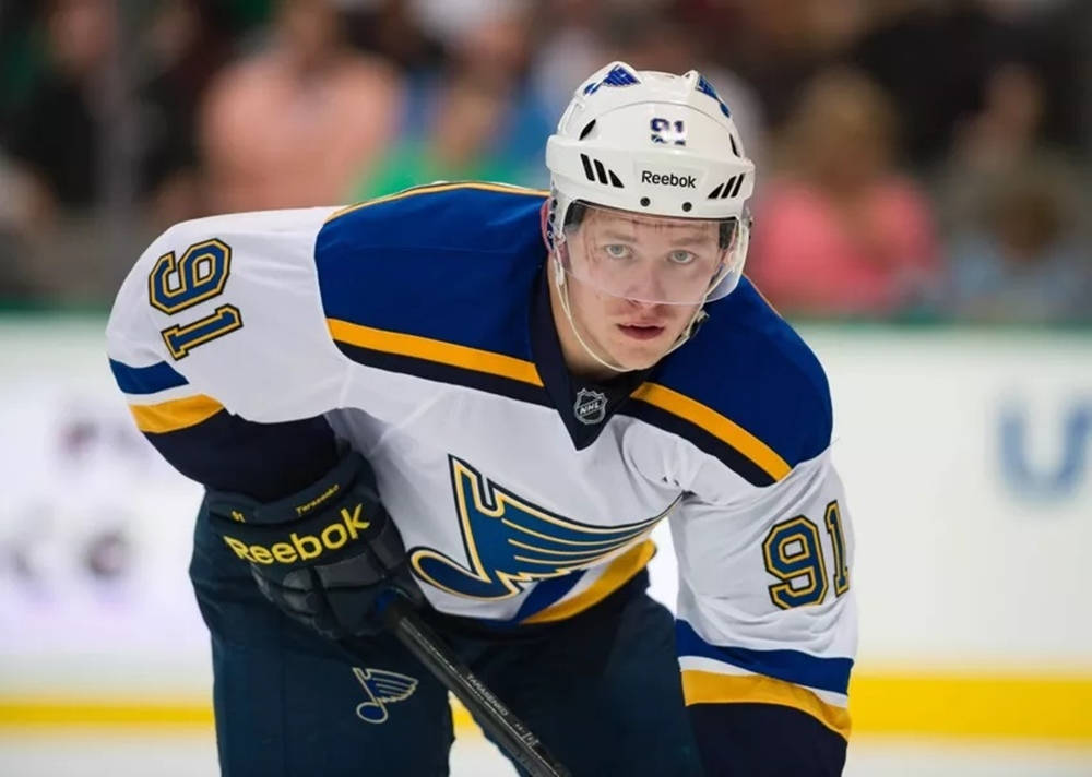 St Louis Blues 桌布 壁紙 — 一名專注的曲棍球運動員身穿聖路易斯藍調球衣，在冰上向前傾身，握著他的球桿。