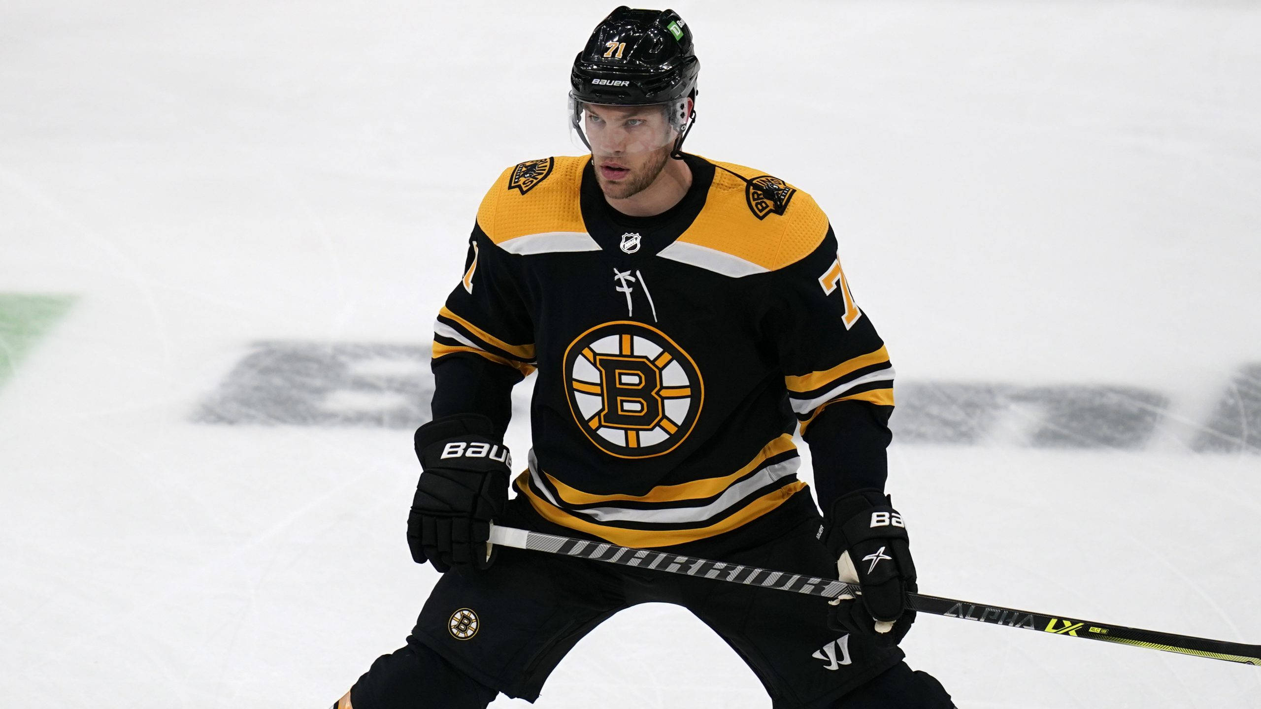 hockey 桌布 壁紙 — 一名專注的曲棍球運動員身穿黑金色Bruins裝備，蹲在冰上握著球棍。