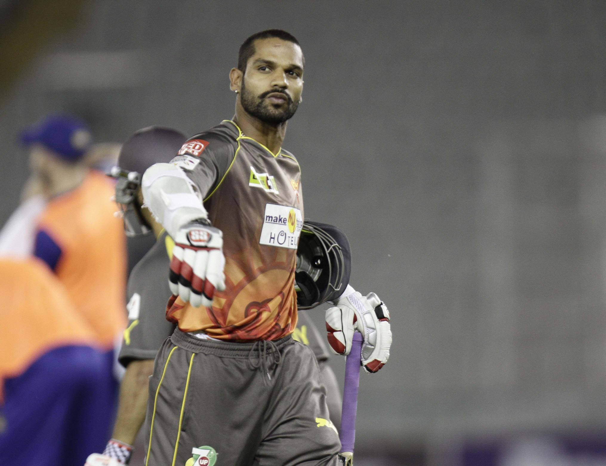 shikhar dhawan 桌布 壁紙 — 一名專注的板球運動員身穿棕色和橙色制服，在夜間的體育場上手持球棒和頭盔。