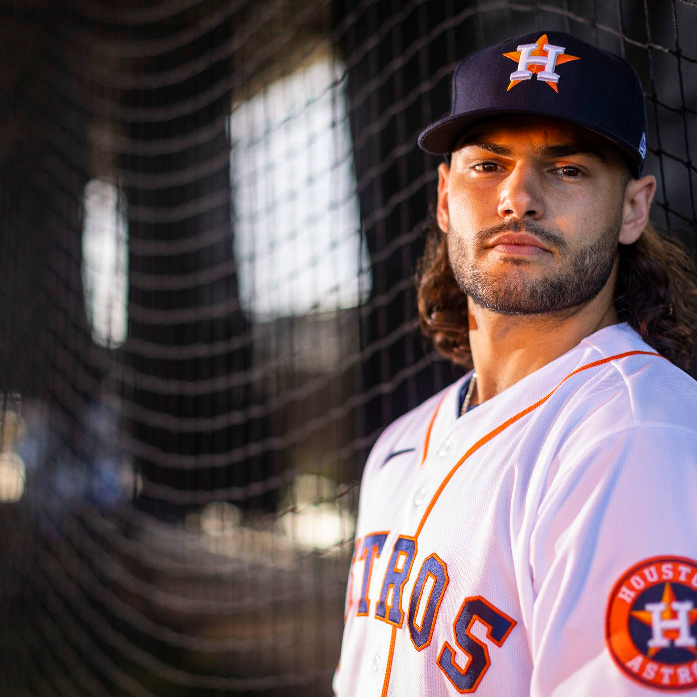 Astros 桌布 壁紙 — 一名專注的棒球運動員身穿休士頓太空人隊制服，站在打擊籠中，陽光透過他身後的網子灑落。