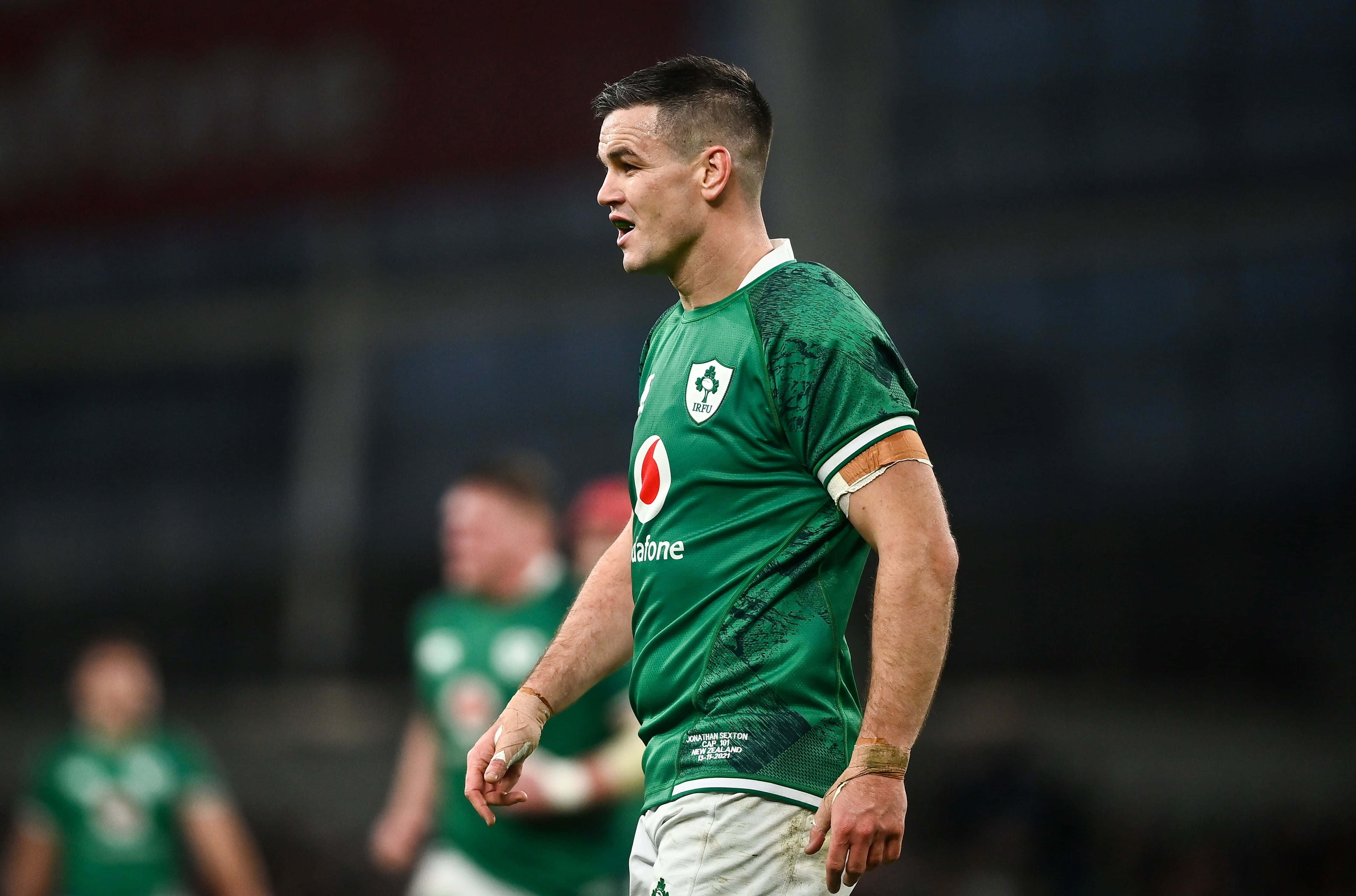 Ireland Rugby 桌布 壁紙 — 一名專注的橄欖球運動員身穿帶有三葉草標誌的綠色球衣，在球場燈光下進行比賽時站在場上。
