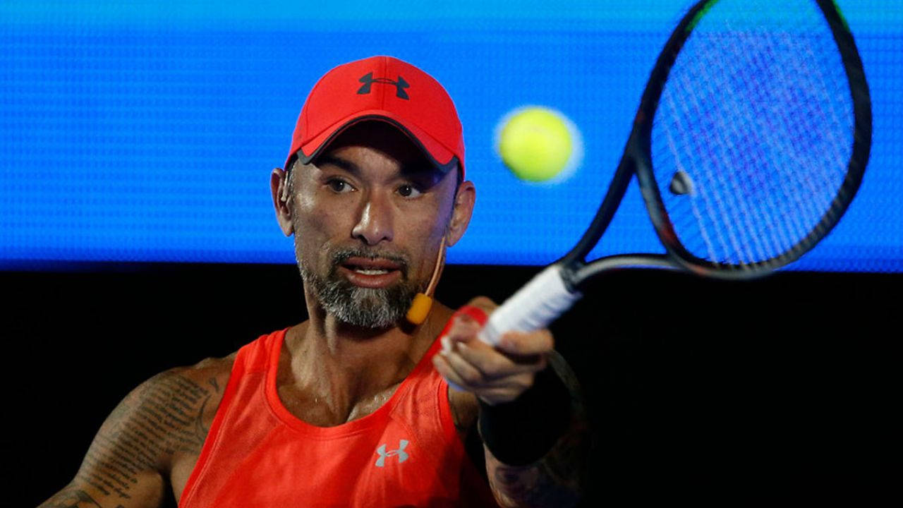 Tennis 桌布 壁紙 — 一名專注的男性網球選手身穿紅色裝備，在藍色螢幕背景前揮拍擊打一顆亮黃色的球。