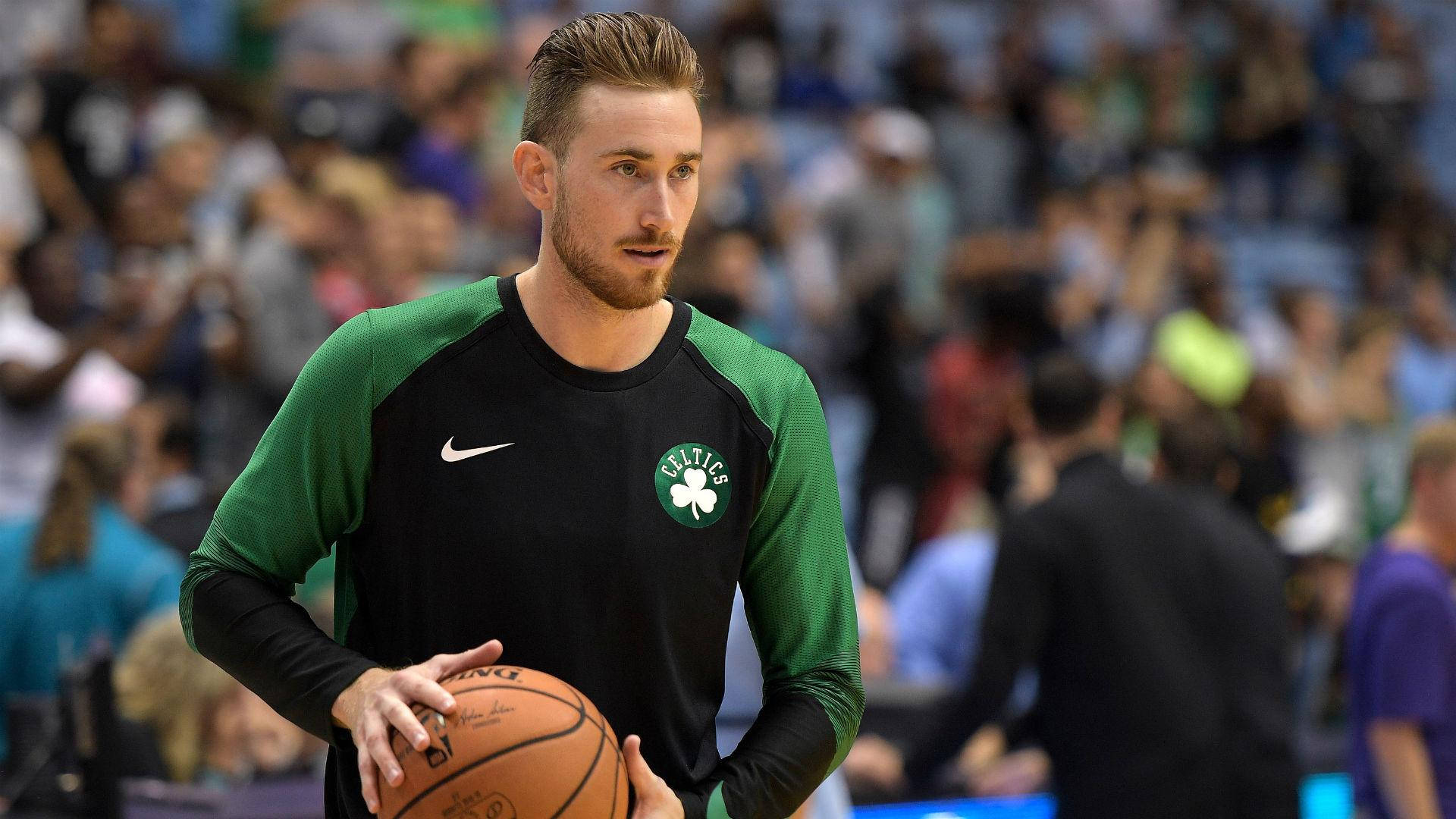 gordon hayward 桌布 壁紙 — 一名專注的籃球運動員穿著綠色和黑色的塞爾提克熱身衫，在球場上拿著球，背景有模糊的觀眾。