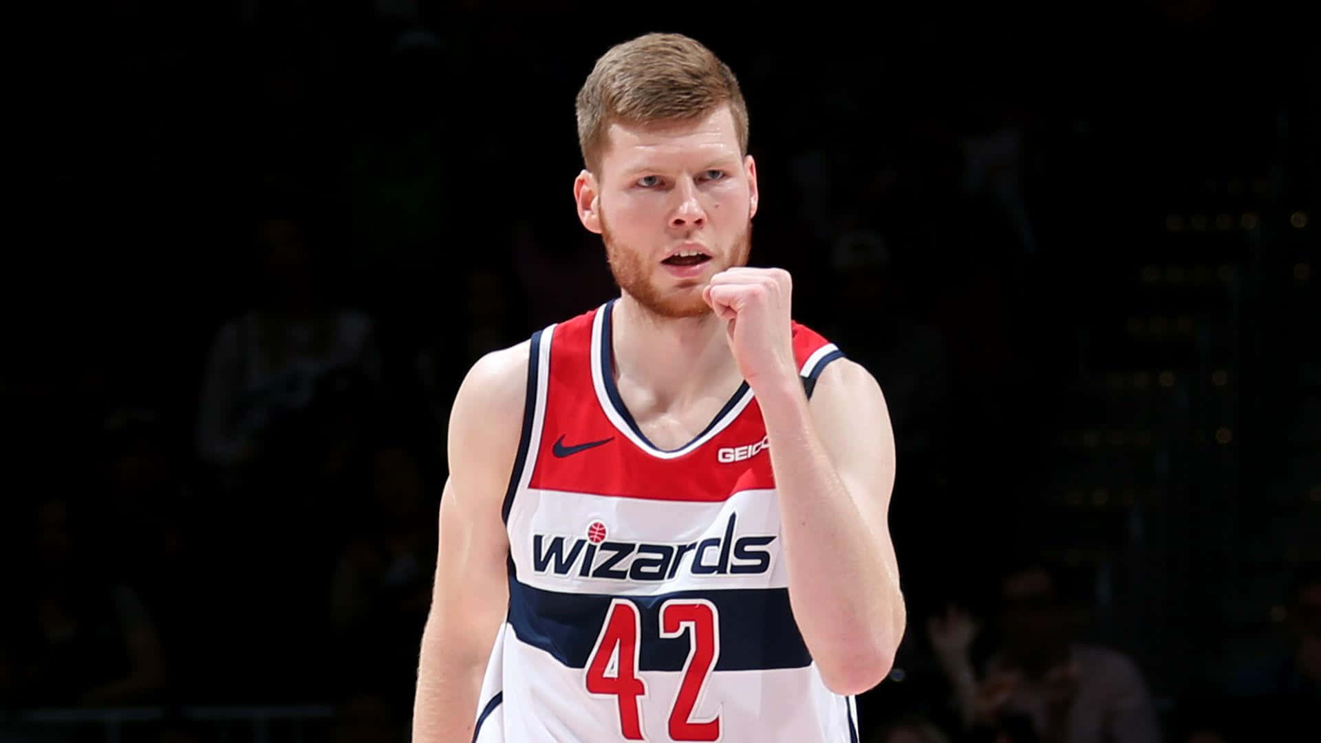 NBA 桌布 壁紙 — 一名專注的籃球運動員身穿巫師隊球衣，在明亮的場館燈光下比賽時舉起拳頭，展現決心。