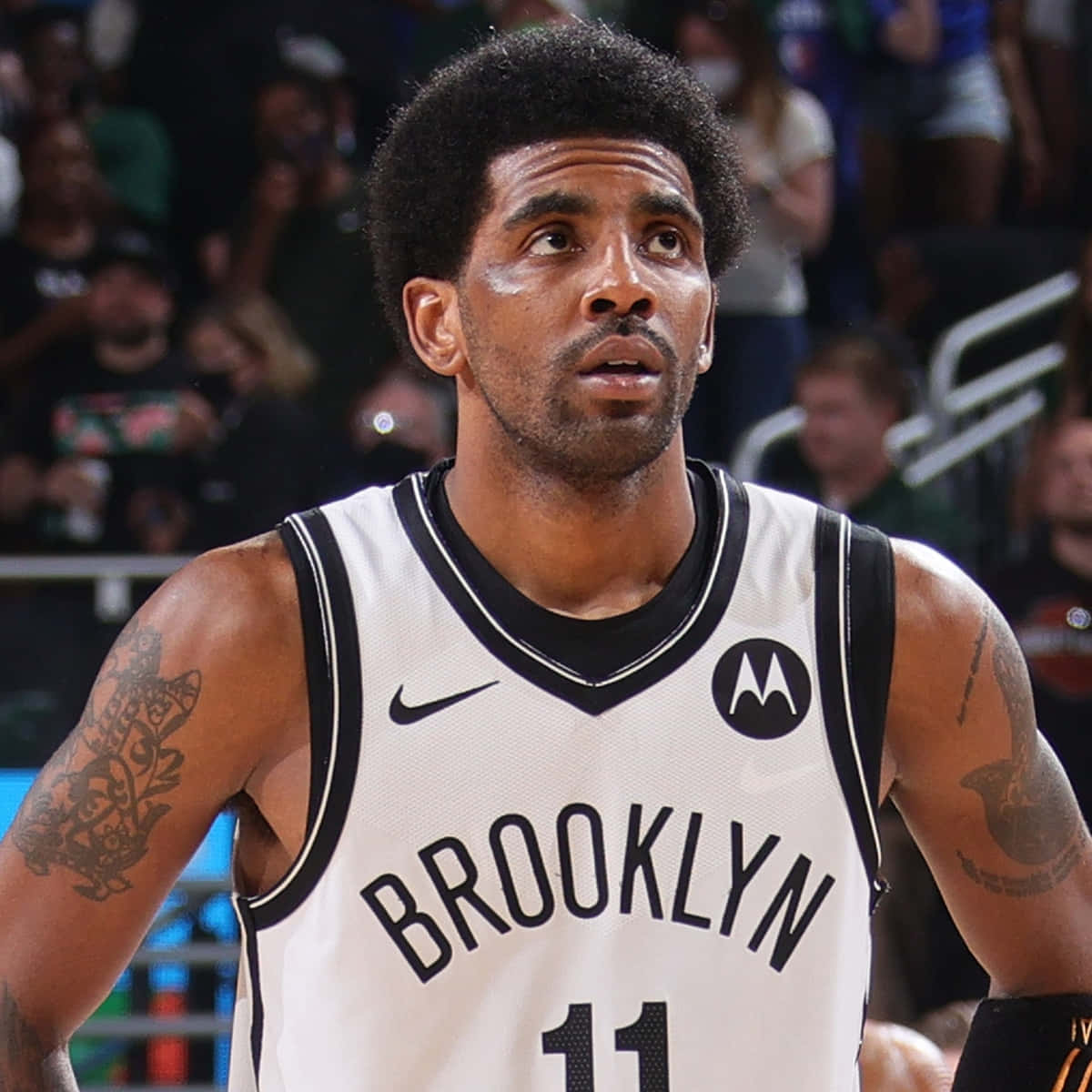 Kyrie Irving Nets 桌布 壁紙 — 一名專注的籃球運動員身穿布魯克林球衣，在比賽中凝視著，背景是模糊的觀眾。
