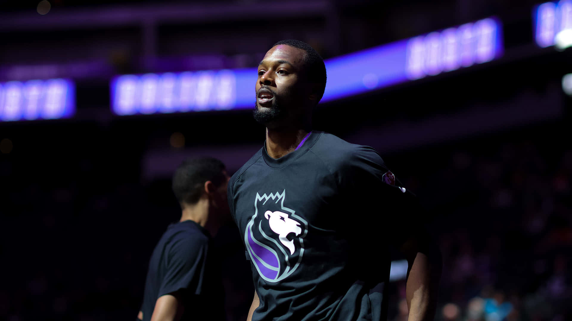NBA 桌布 壁紙 — 一名專注的籃球運動員身穿深色球衣，帶有紫色和白色標誌，在比賽期間站在場館燈光下。