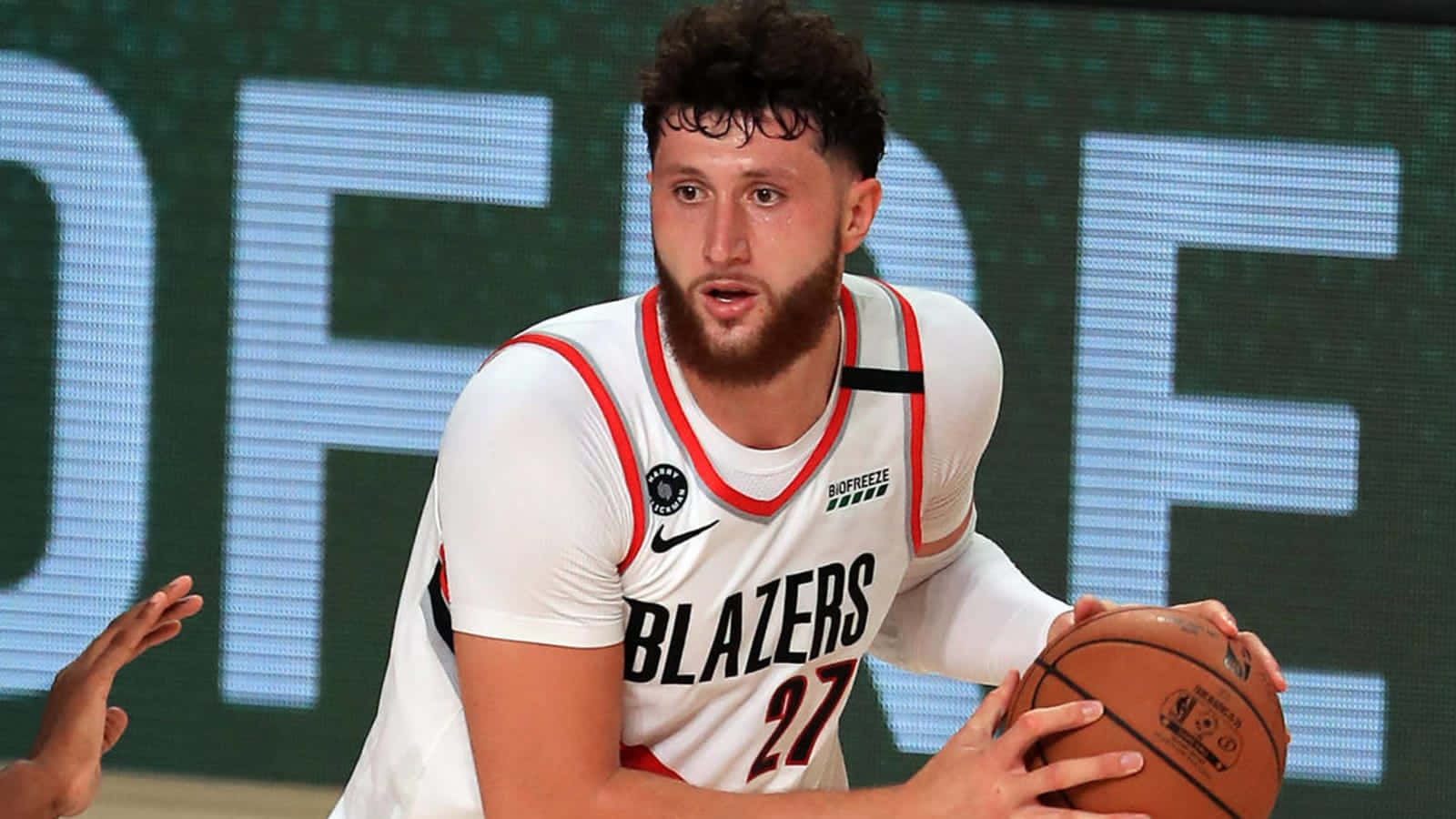 籃球 桌布 壁紙 — 一名專注的籃球運動員身穿白色 Blazers 球衣，在比賽中持球，背景為電子記分板。