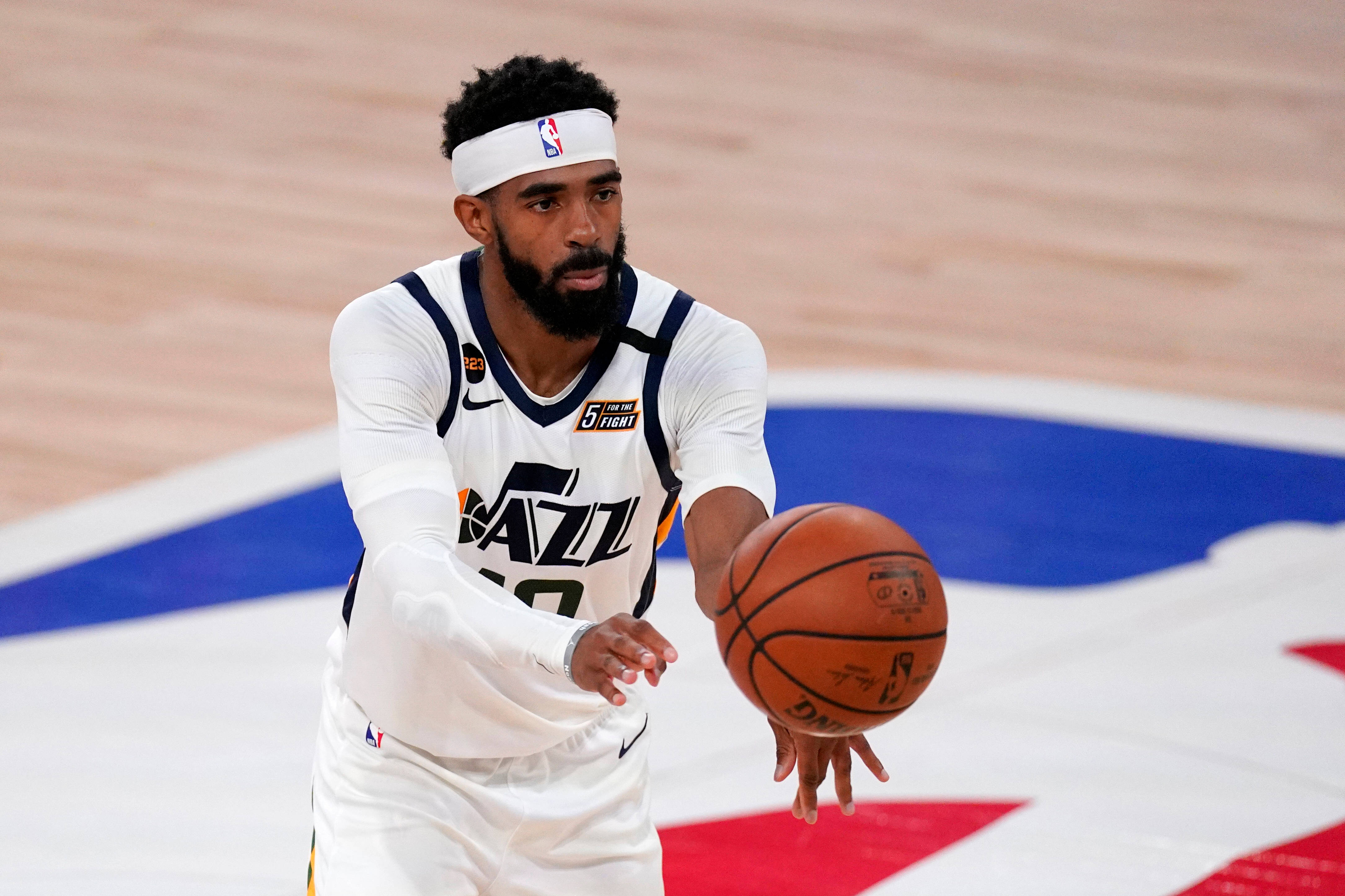 mike conley 桌布 壁紙 — 一名專注的籃球運動員身穿白色爵士隊球衣，在光滑的球場上運球，球場上有醒目的球隊標誌。