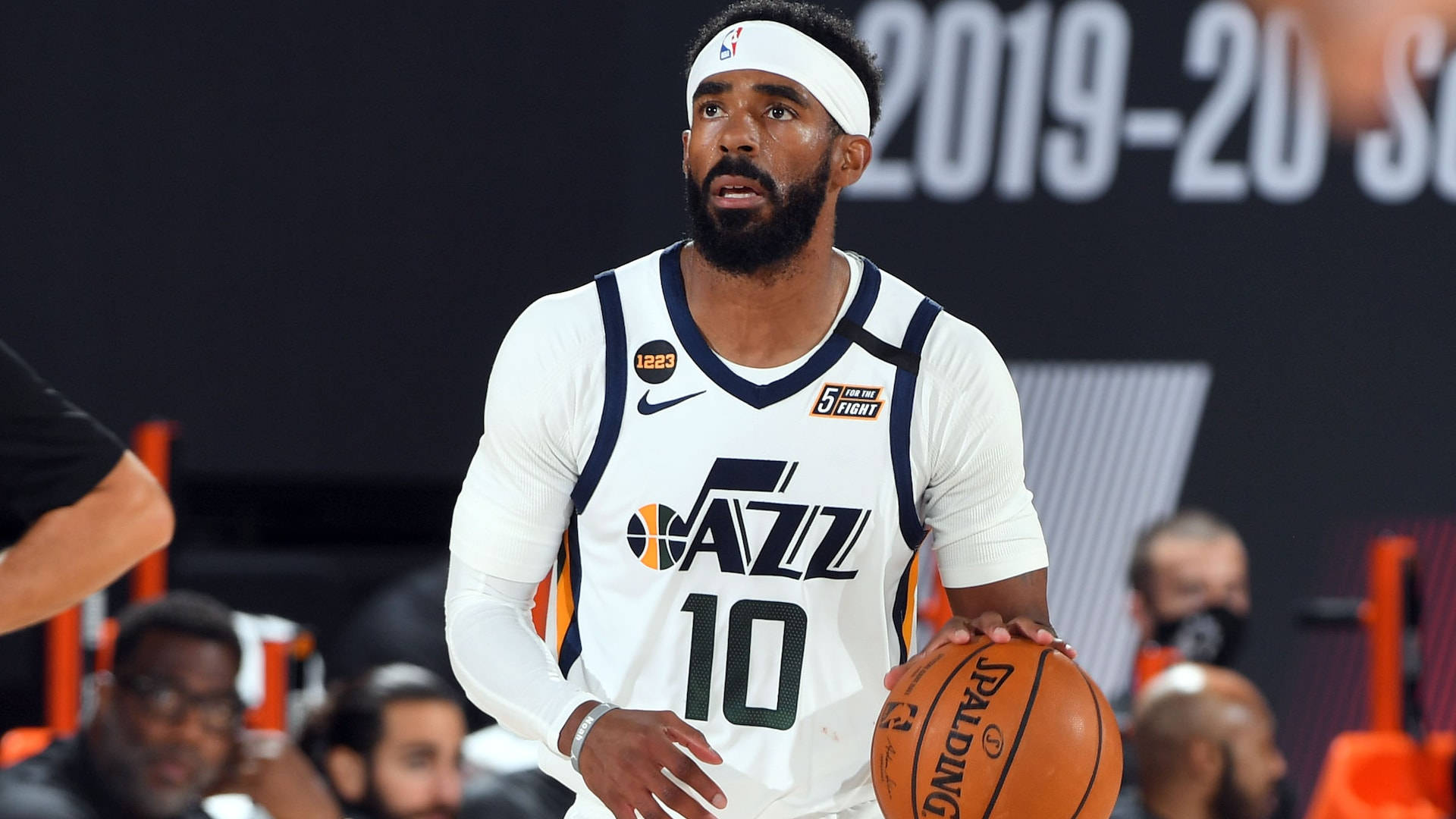 mike conley 桌布 壁紙 — 一名專注的籃球運動員身穿白色爵士隊球衣，在明亮的場館燈光下於比賽中手持Spalding籃球。