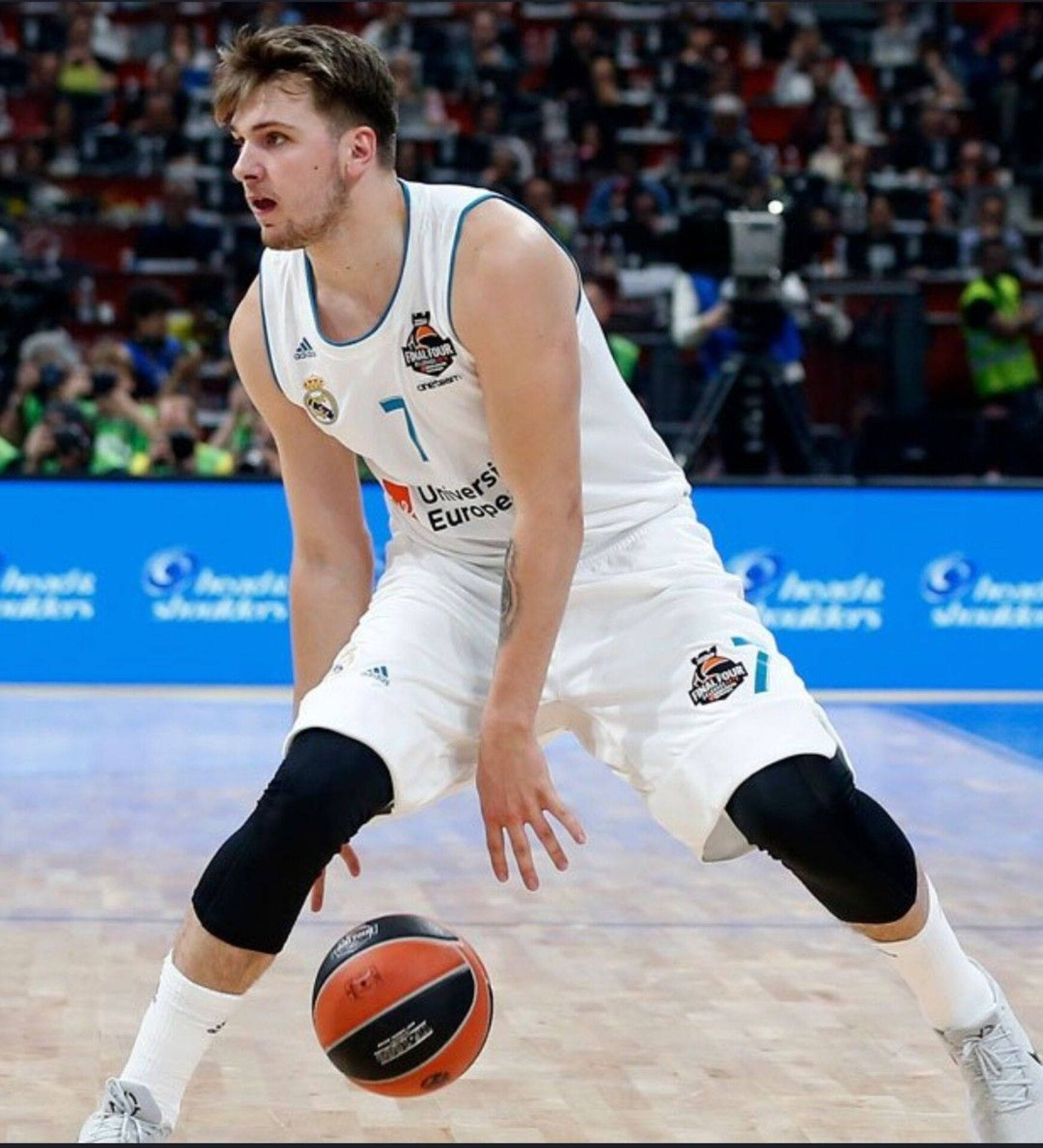 Luka 桌布 壁紙 — 一名專注的籃球運動員身穿白色球衣，在明亮的場館燈光下於激烈比賽中低運球。
