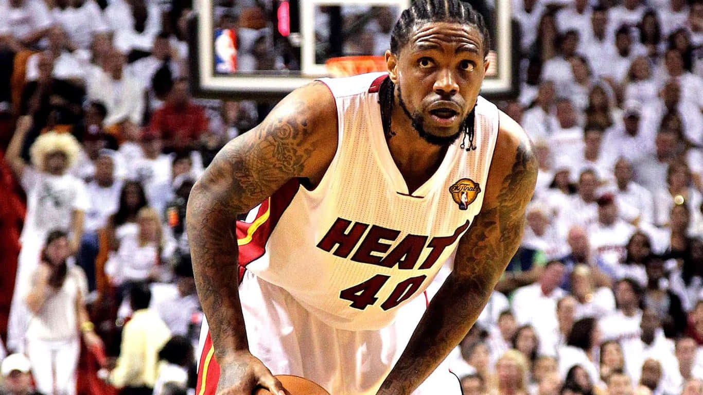 Udonis Haslem 桌布 壁紙 — 一名專注的籃球運動員身穿白色邁阿密熱火隊球衣，在滿場觀眾的背景下於激烈比賽中運球。