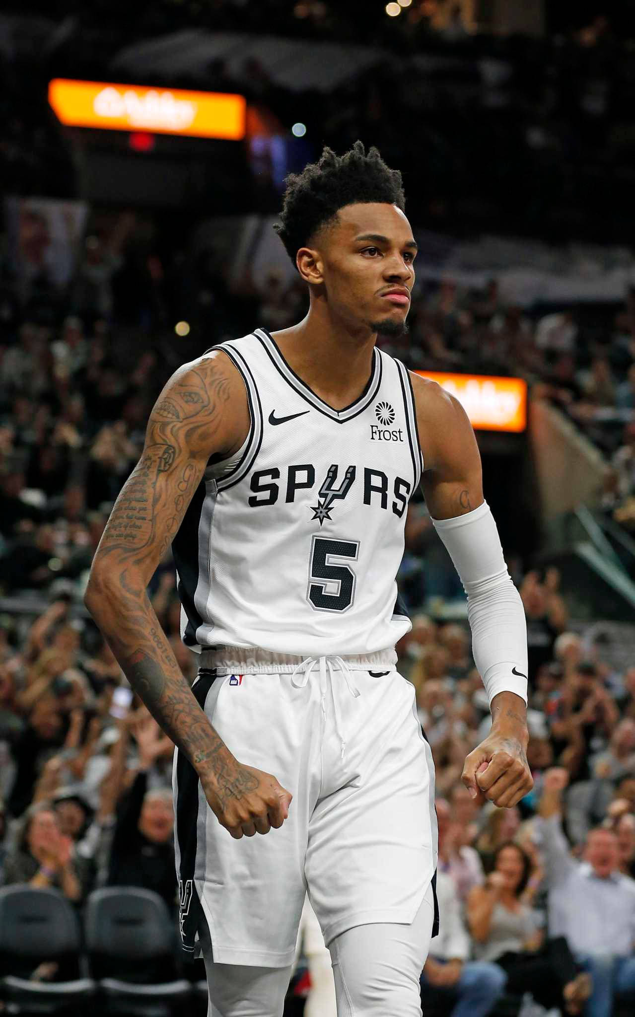 Dejounte Murray 桌布 壁紙 — 一名專注的籃球運動員身穿白色馬刺隊5號球衣，在燈光明亮的球場上行走，周圍是歡呼的球迷。