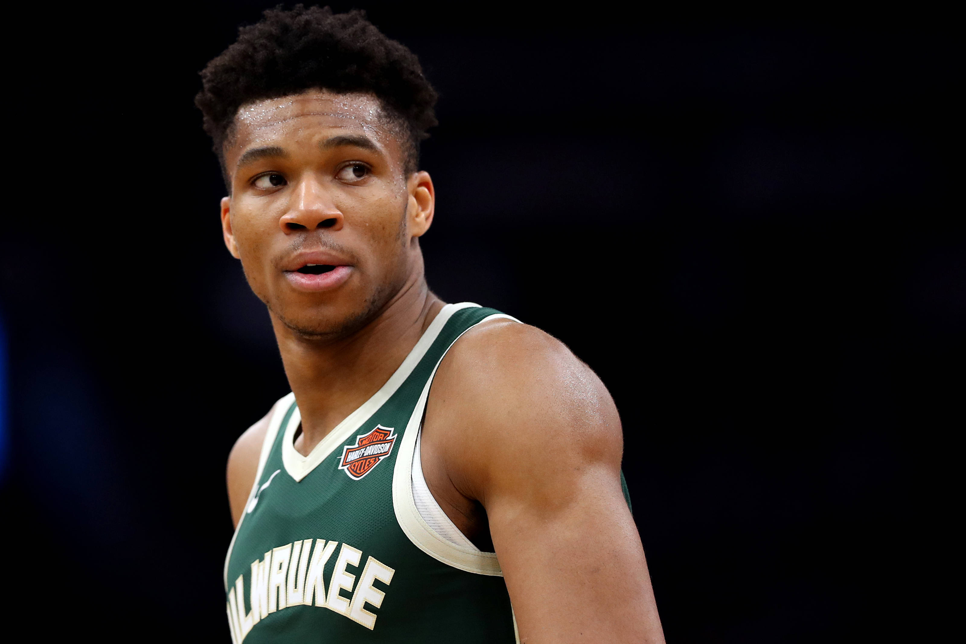 Giannis 桌布 壁紙 — 一名專注的籃球運動員身穿綠色密爾瓦基球衣，在深色背景下專注地望向鏡頭外。