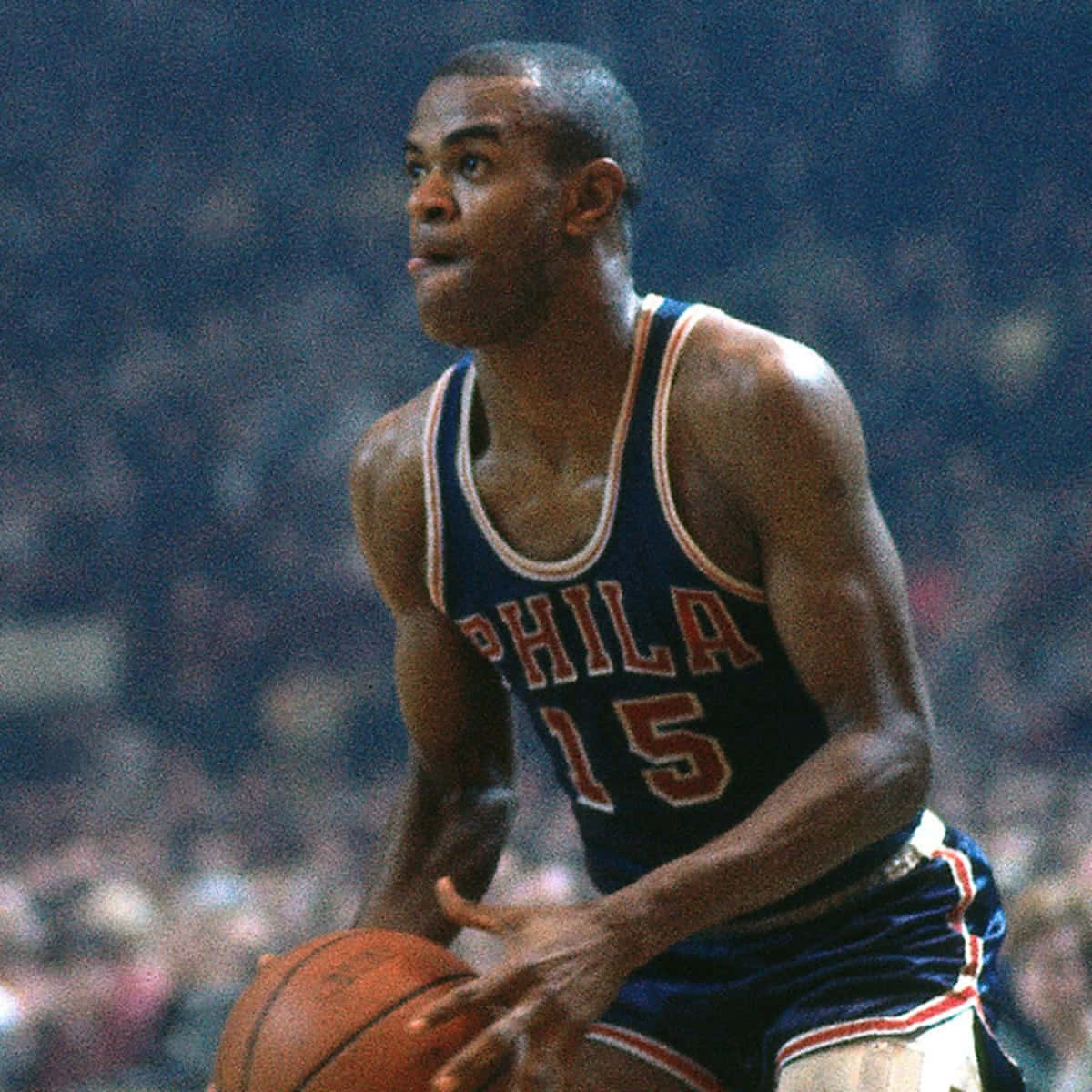 NBA 桌布 壁紙 — 一名專注的籃球運動員身穿藍色「PHILA 15」球衣，在場館燈光下比賽中激烈運球。