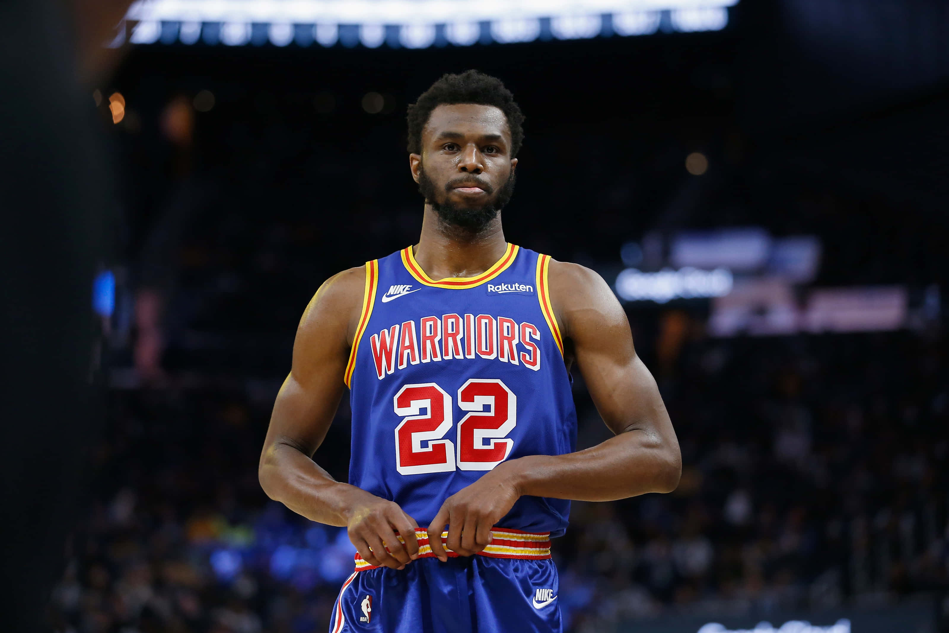 Andrew Wiggins 桌布 壁紙 — 一名專注的籃球運動員身穿藍色勇士隊22號球衣，在比賽期間站在燈光明亮的球場上。