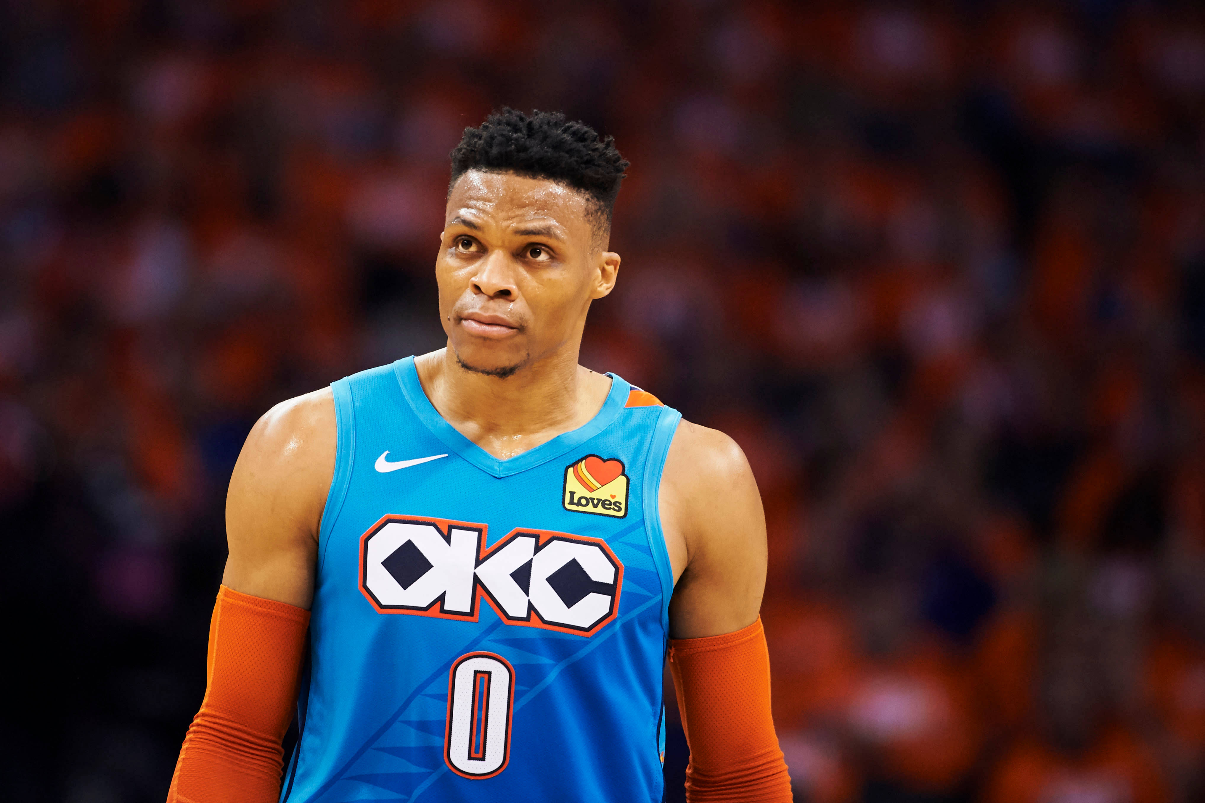 Westbrook 桌布 壁紙 — 一名專注的籃球運動員身穿藍色和橙色OKC球衣，站在球場上，背景是模糊的人群。