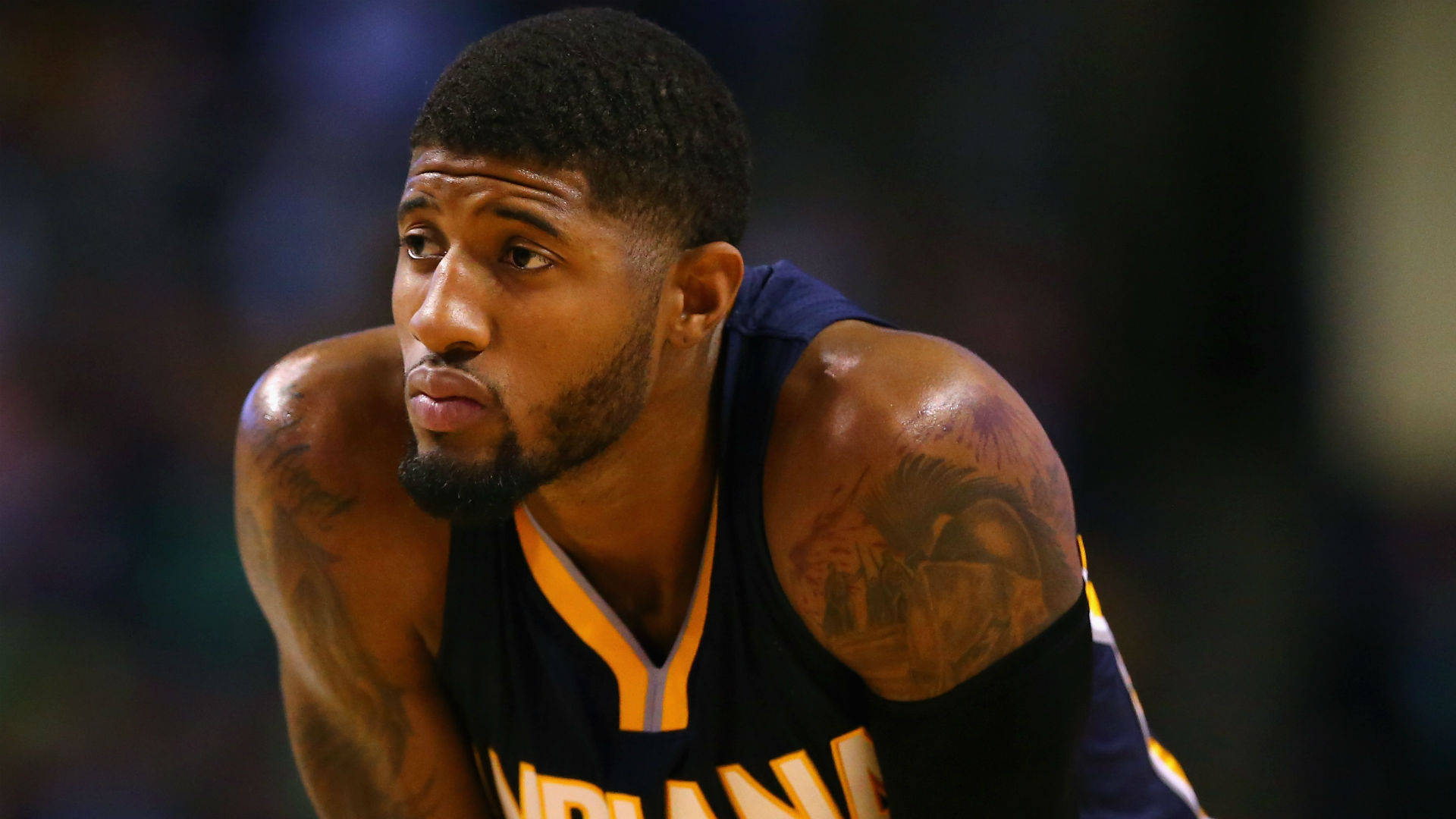 Paul George 桌布 壁紙 — 一名專注的籃球運動員身穿藍色和金色球衣，身體前傾，手臂上的刺青清晰可見。