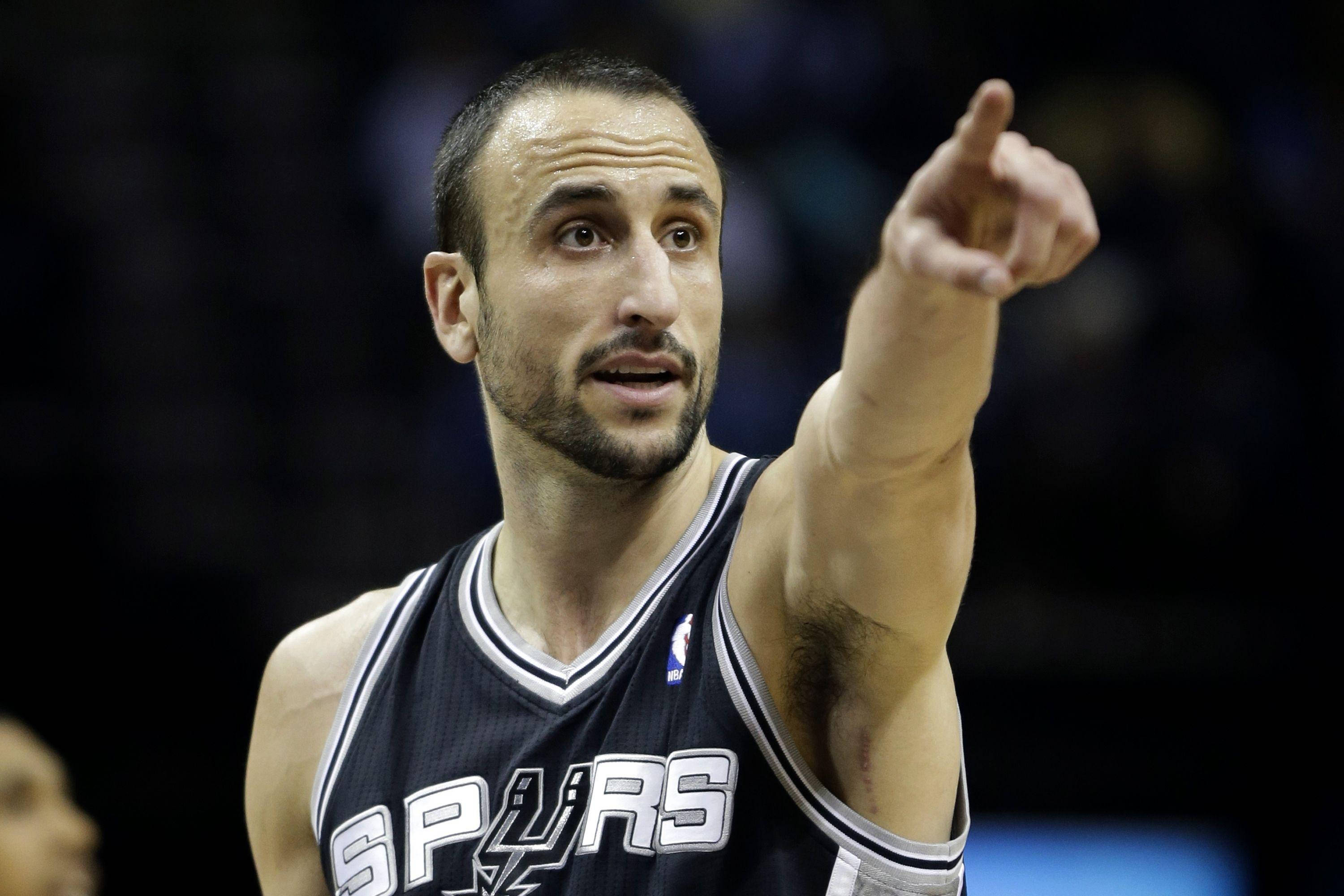 Manu 桌布 壁紙 — 一名專注的籃球運動員身穿馬刺隊球衣，在明亮的場館燈光下於比賽中專注地指向某處。