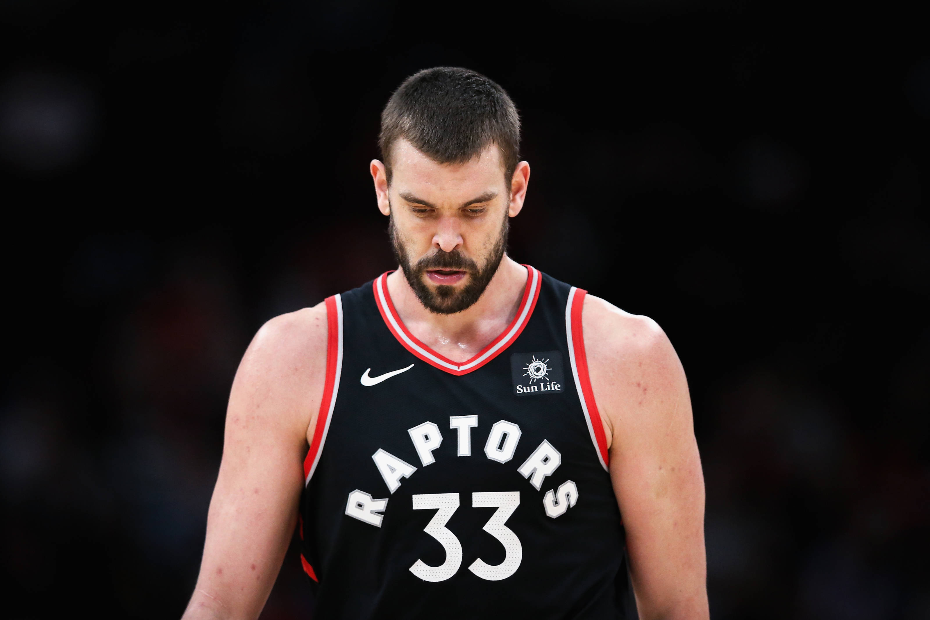 Marc Gasol 桌布 壁紙 — 一名專注的籃球運動員身穿黑色Raptors球衣，號碼33，在黑暗模糊的背景前低頭，表情嚴肅。
