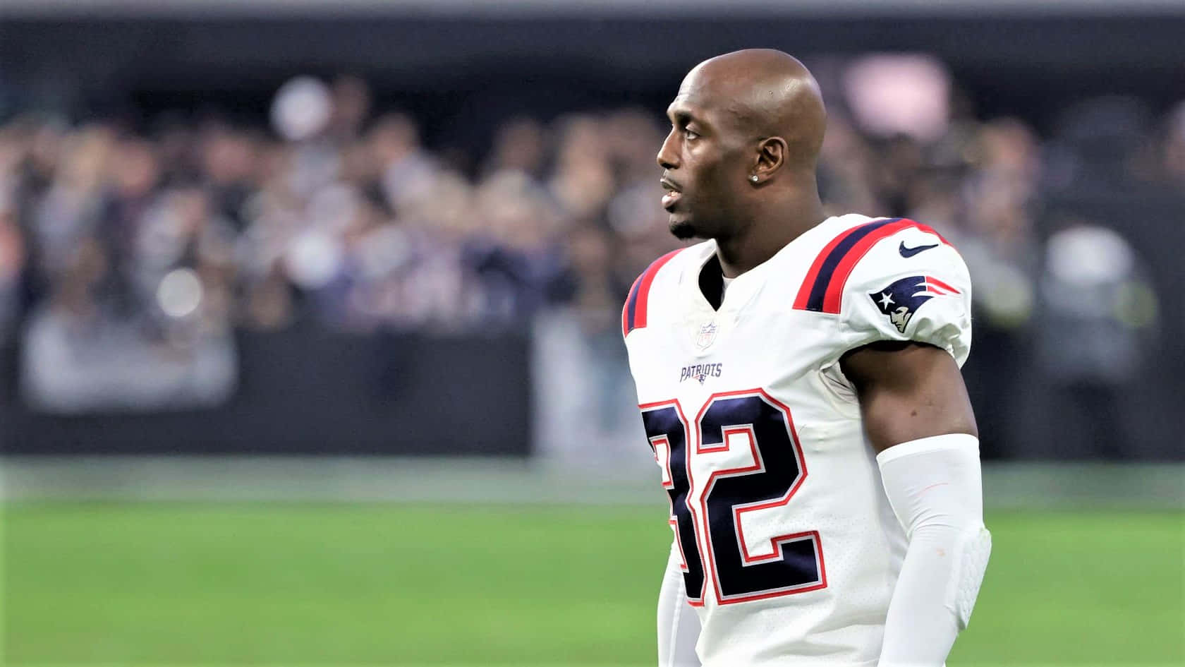 Devin Mccourty 桌布 壁紙 — 一名專注的美式足球員身穿白色Patriots球衣，號碼32，站在綠色球場上，球場燈光下。