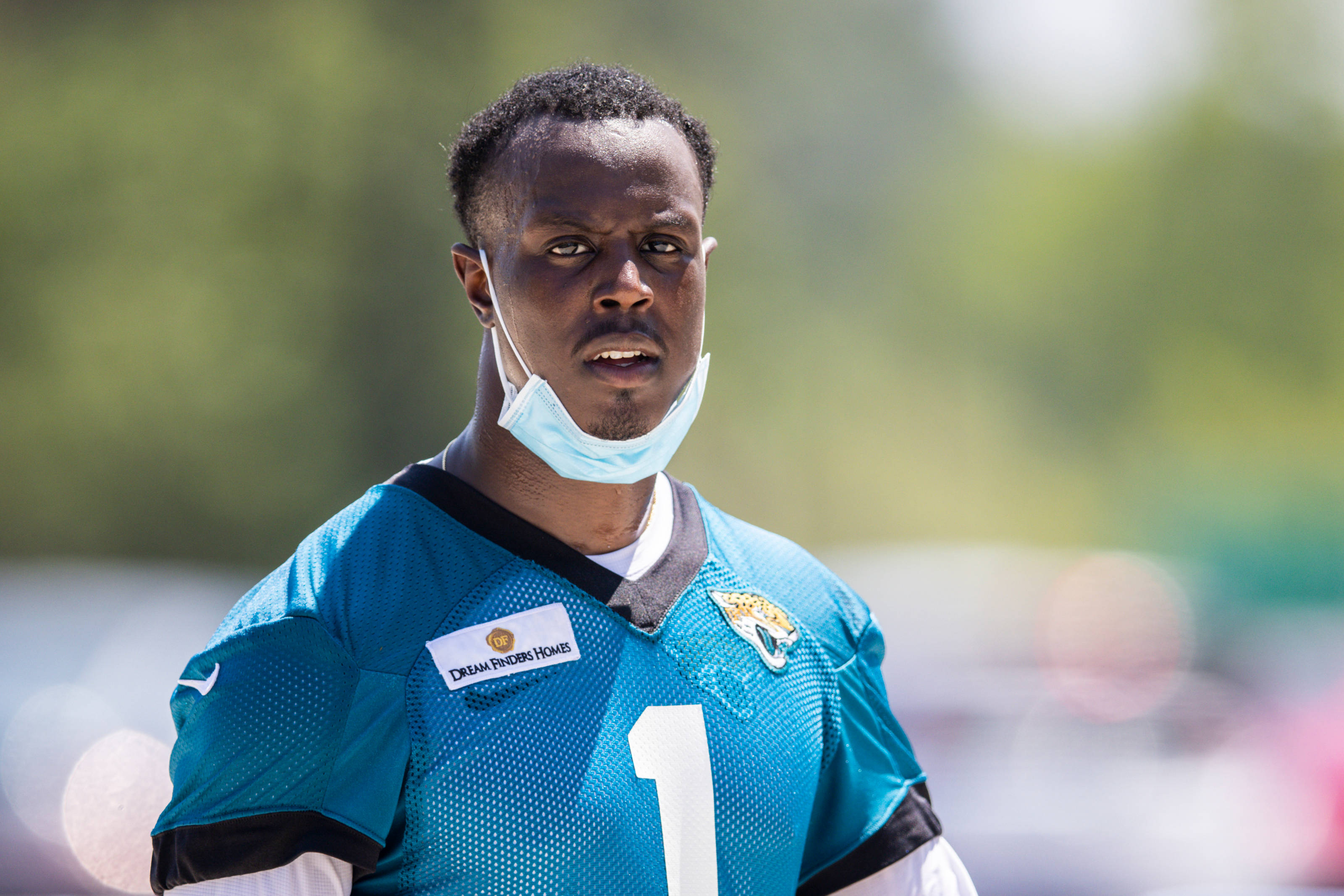Travis Etienne 桌布 壁紙 — 一名專注的美式足球員身穿青綠色球衣，號碼為一，在明亮的陽光下戶外站立，背景為模糊的綠色。