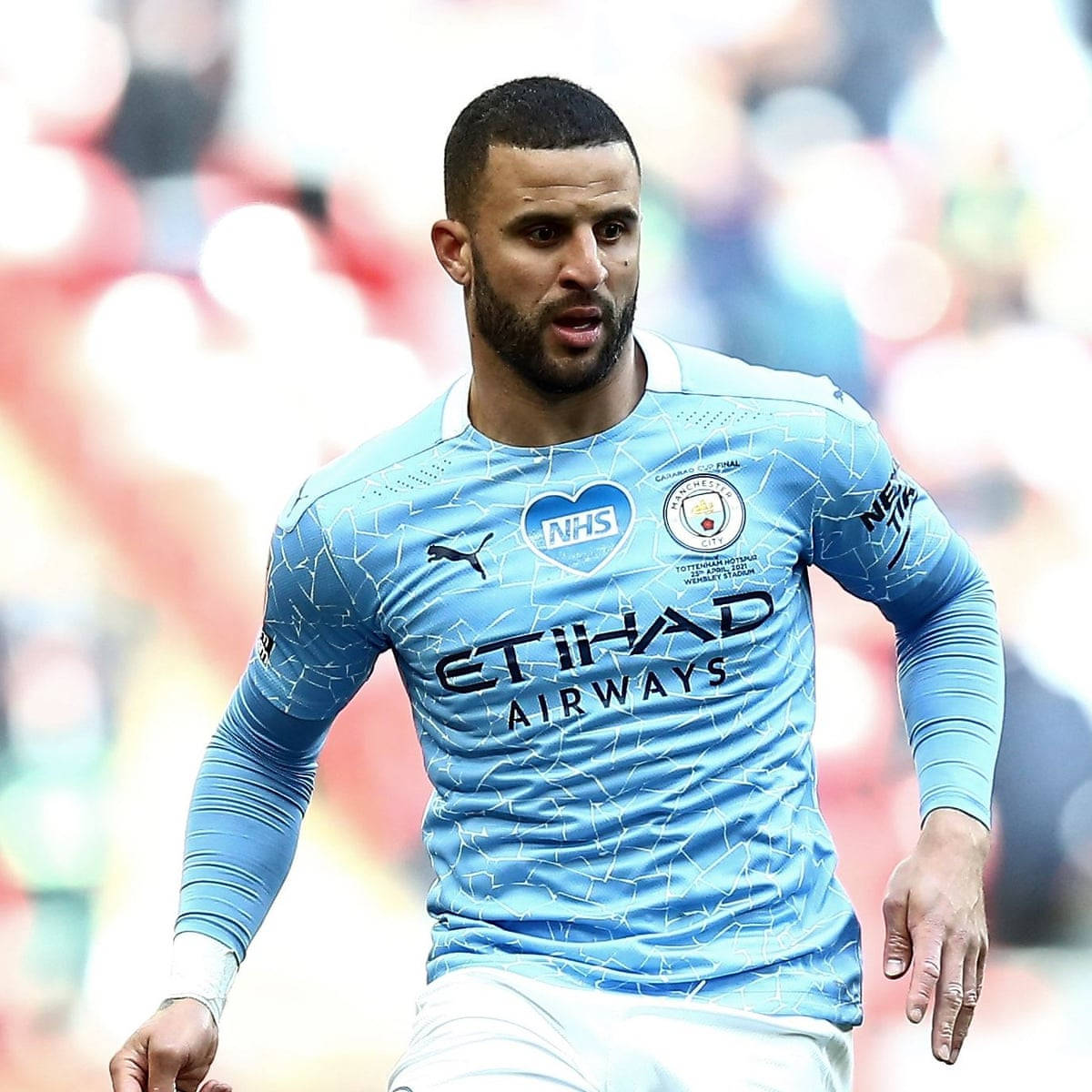 Kyle Walker 桌布 壁紙 — 一名專注的足球員身穿淺藍色曼城球衣，在陽光明媚的球場上衝刺，背景是模糊的觀眾。