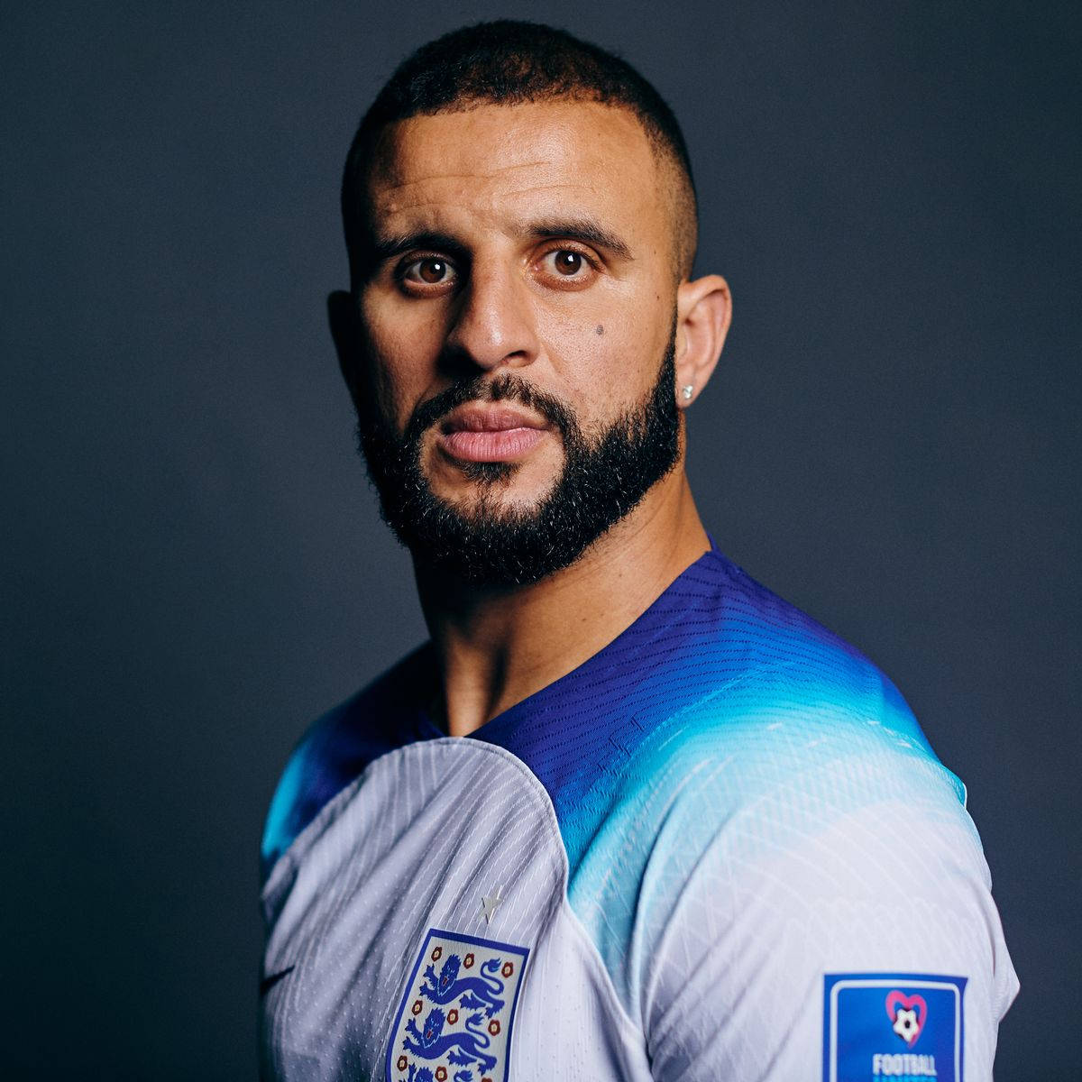 Kyle Walker 桌布 壁紙 — 一名專注的足球員身穿英格蘭球衣，在黑暗的攝影棚背景下凝視著。