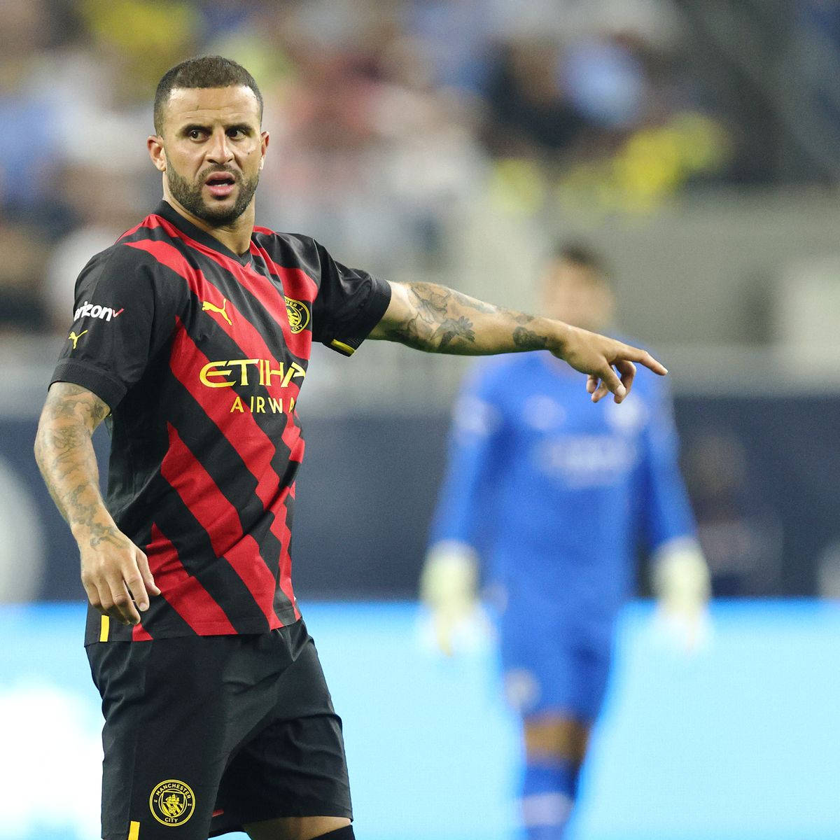 Kyle Walker 桌布 壁紙 — 一名專注的足球運動員身穿紅黑橫條球衣，在夜間比賽的球場燈光下激烈地做手勢。