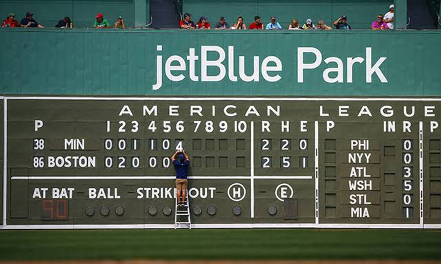 運動 桌布 壁紙 — 一名工人在梯子上更新jetBlue Park的記分板，期間有棒球比賽進行，觀眾在看台觀看。