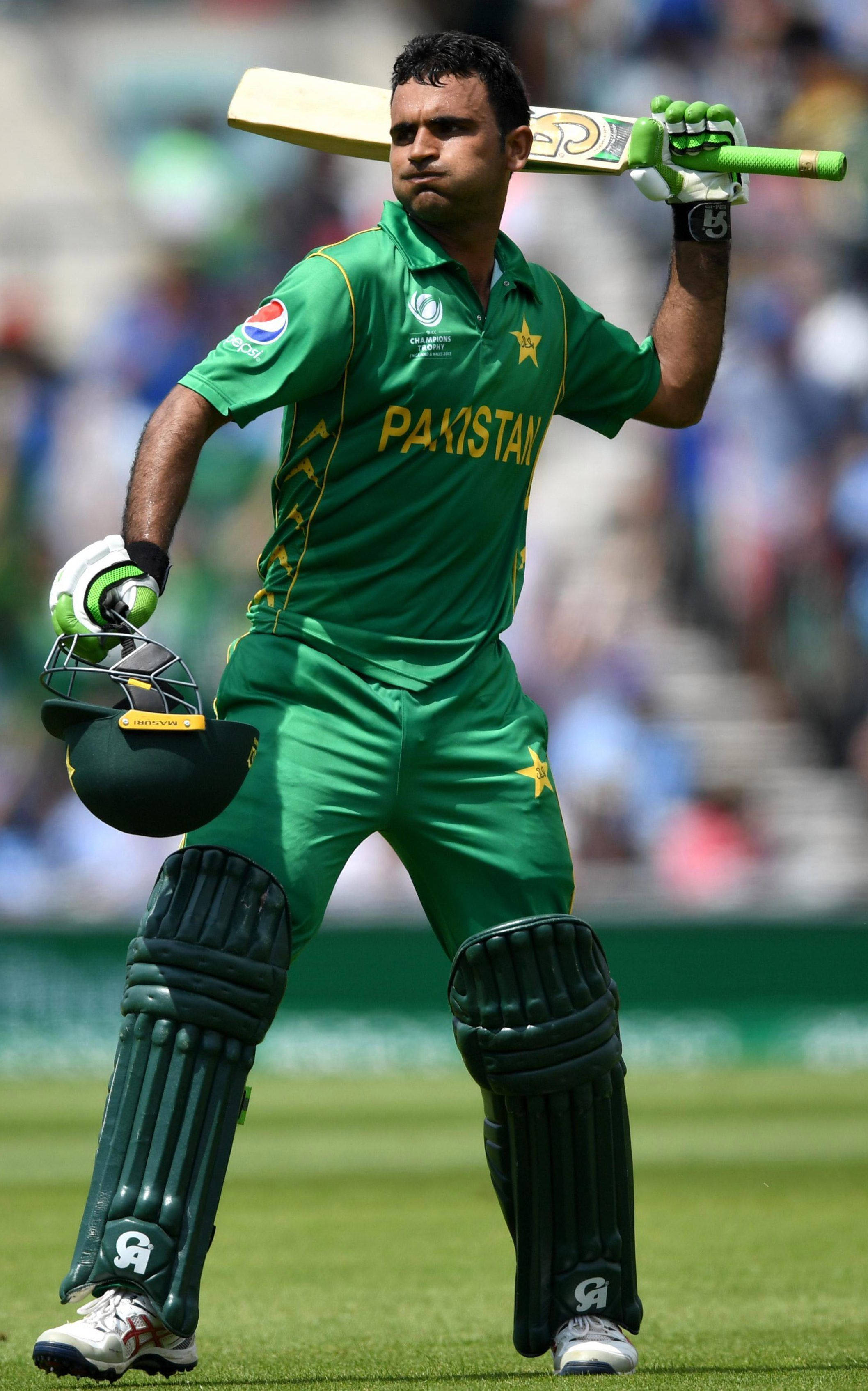 Fakhar Zaman 桌布 壁紙 — 一名巴基斯坦板球運動員穿著綠色制服，在陽光明媚的球場上比賽時手持球棒和頭盔。