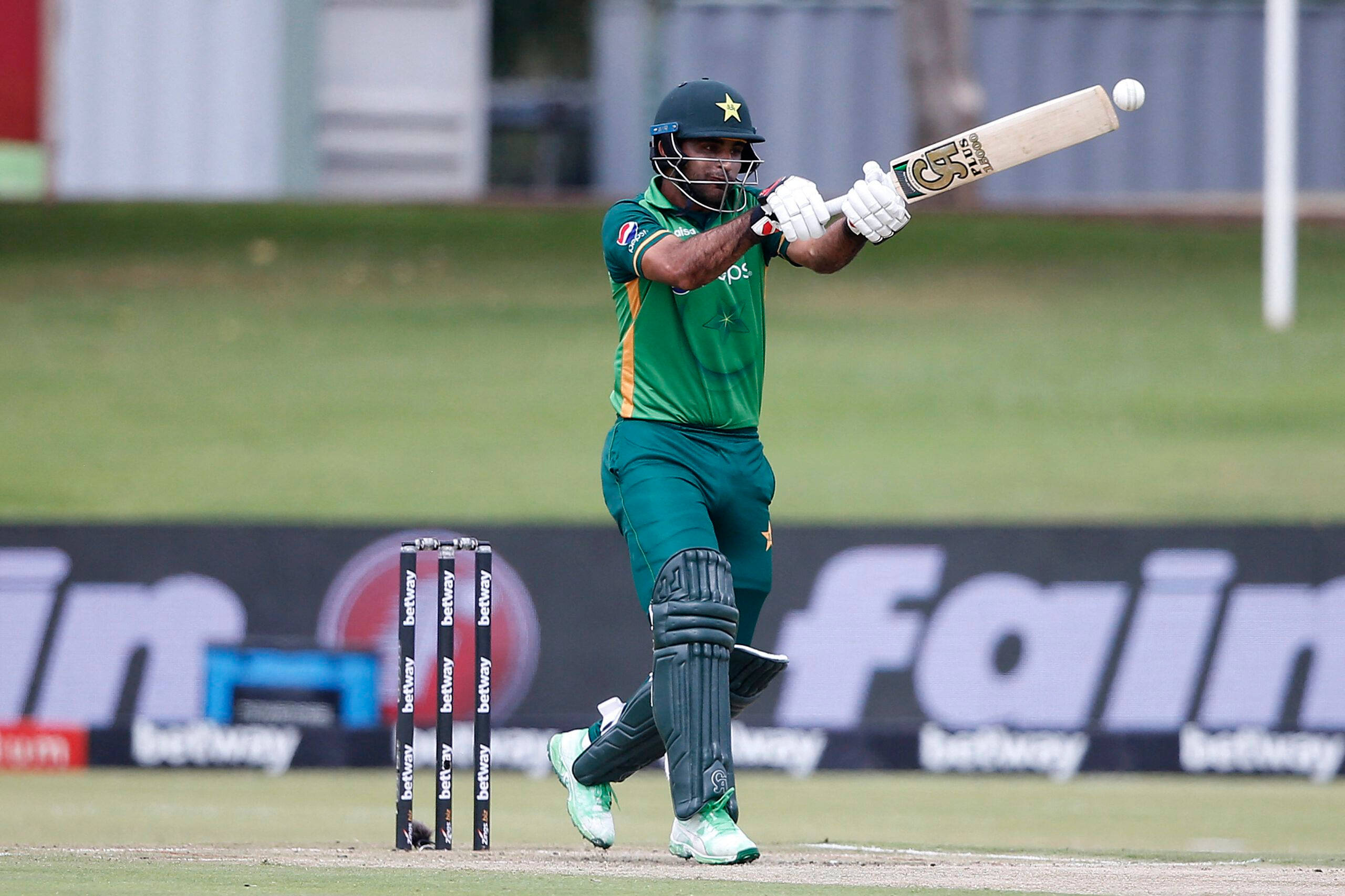 Fakhar Zaman 桌布 壁紙 — 一名巴基斯坦板球運動員身穿綠色制服，在草地場地的日間比賽中揮動球棒擊打白色球。