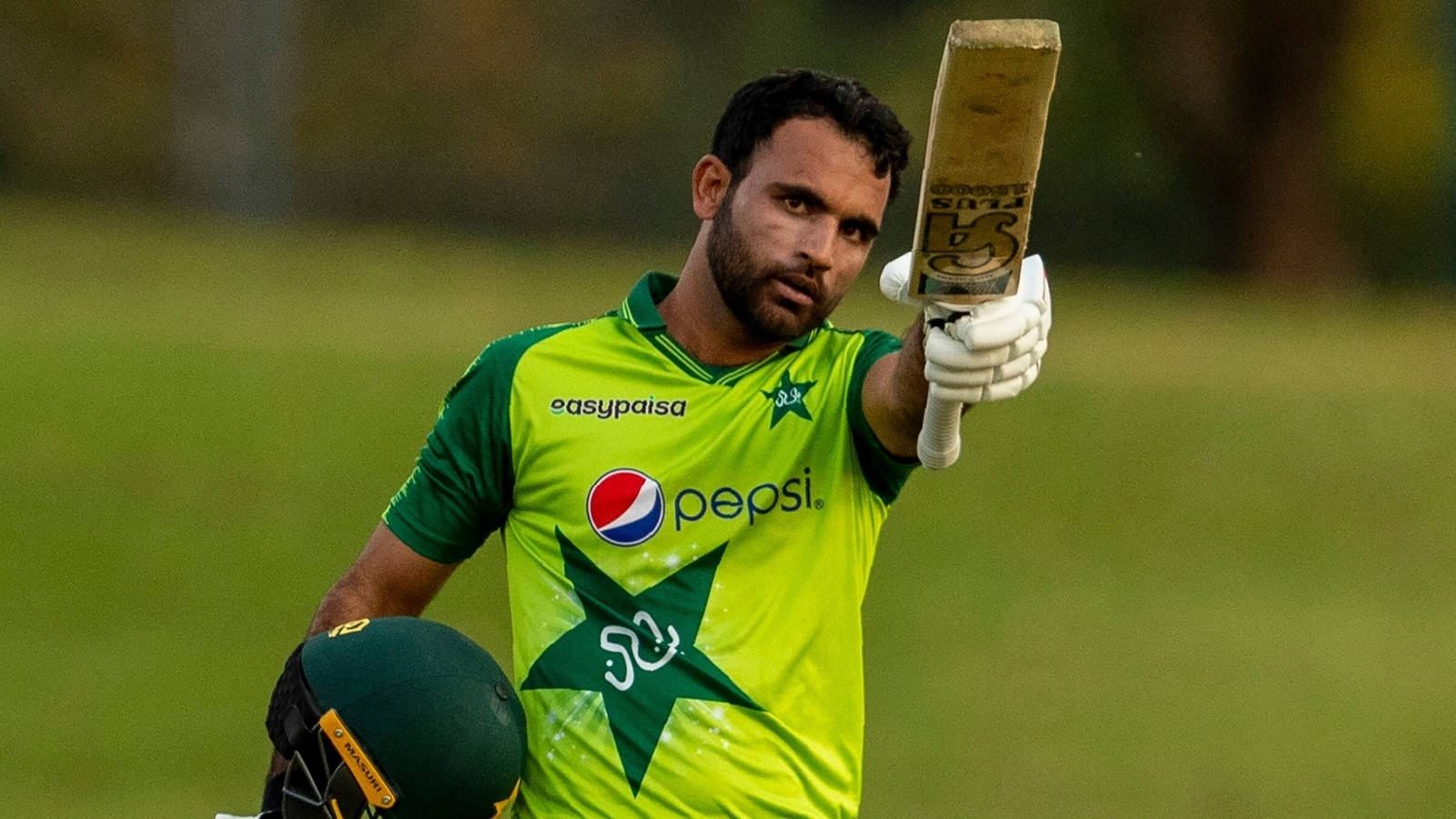Fakhar Zaman 桌布 壁紙 — 一名巴基斯坦板球運動員身穿鮮綠色球衣，在草地上專注地高舉球棒。