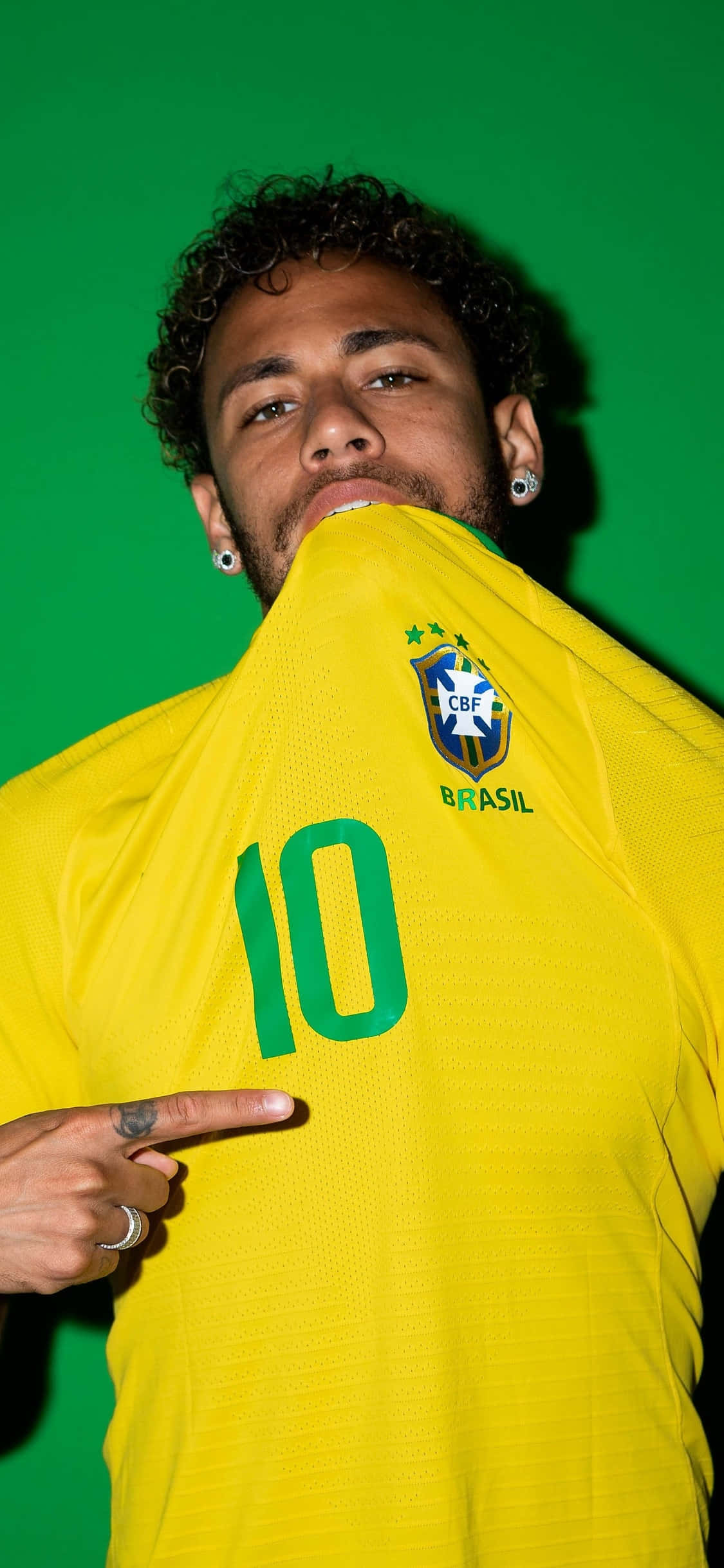 Neymar iPhone 桌布 壁紙 — 一名巴西足球員身穿黃色球衣，背號10，指著球衣，背景為純綠色。