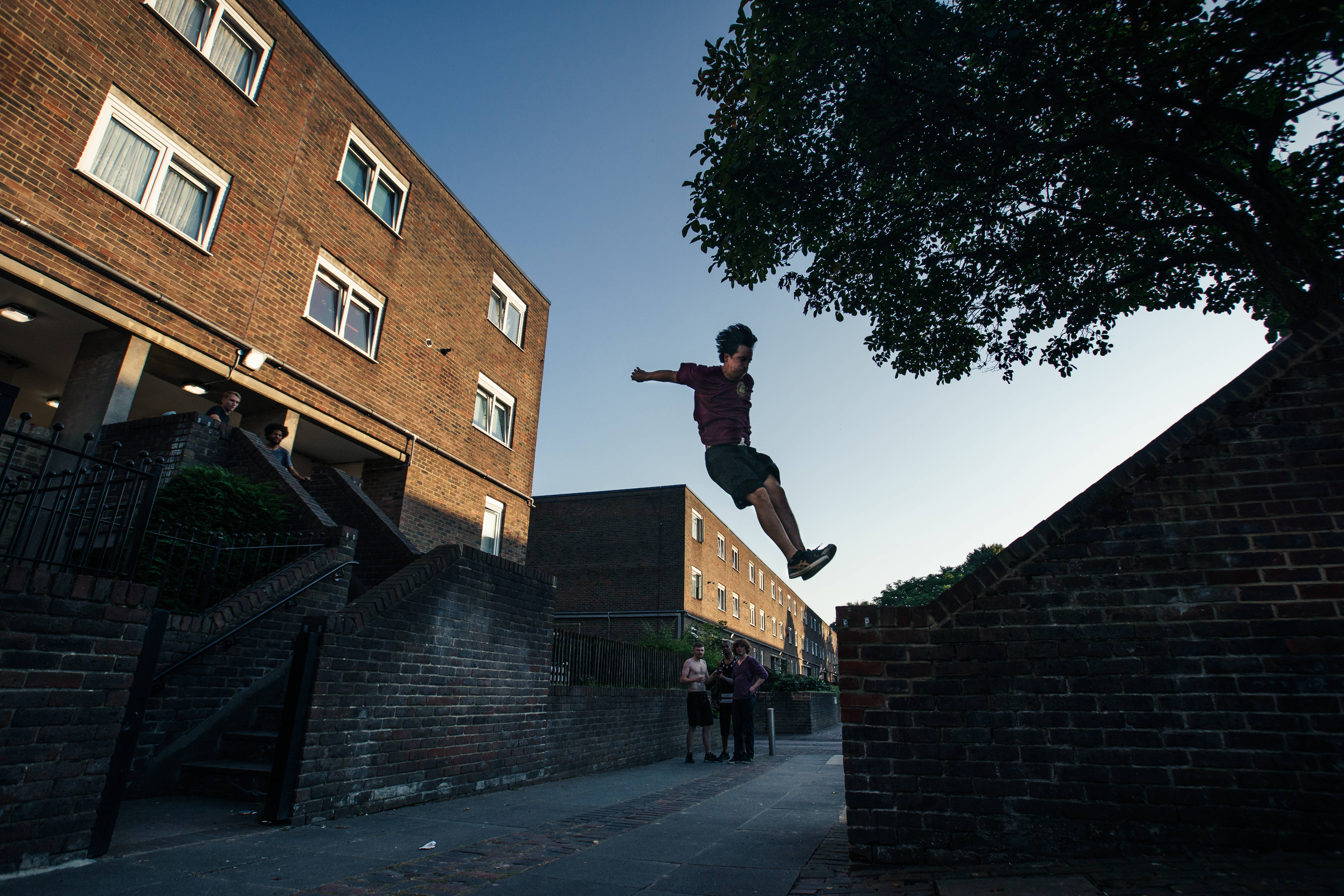 Parkour 桌布 壁紙 — 一名年輕人在黃昏時分的城市小巷中，凌空跳過磚牆。