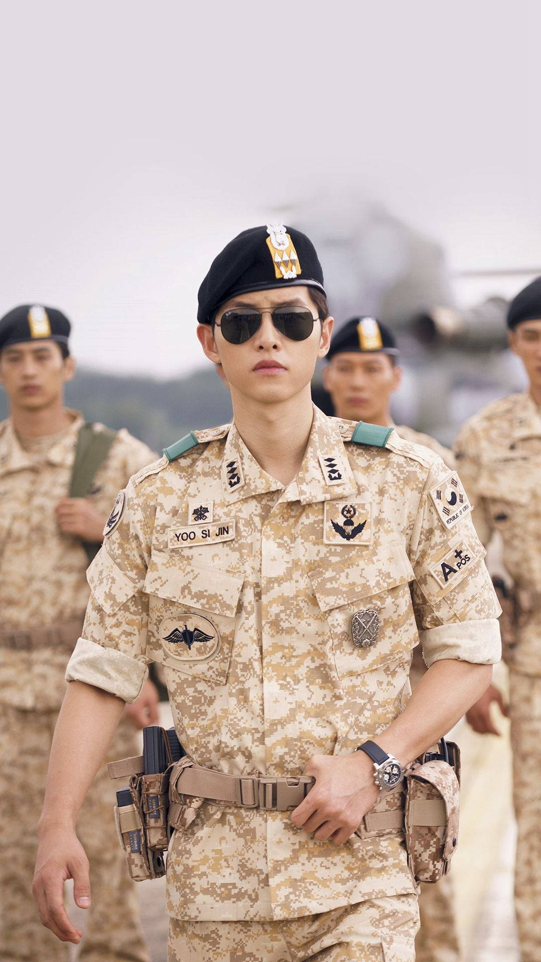 drama 桌布 壁紙 — 一名年輕士兵穿著沙漠迷彩制服和太陽眼鏡，雙手放在腰帶上自信地站著，其他士兵站在他身後。