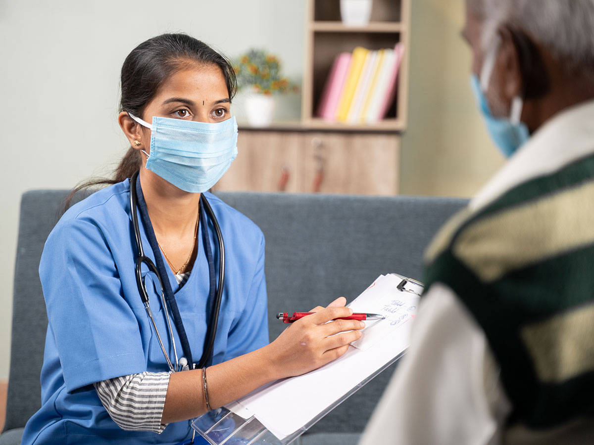 Nurse 桌布 壁紙 — 一名年輕女護士穿著藍色手術衣和口罩，在病人諮詢期間專心聆聽並在記事板上寫筆記。