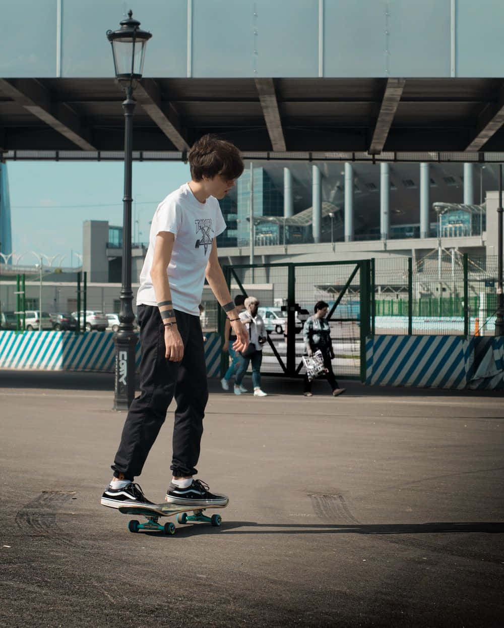 Skater Boy 桌布 壁紙 — 一名年輕滑板手在現代玻璃天篷下，於陽光明媚的城市街道上平穩滑行，背景有行人。