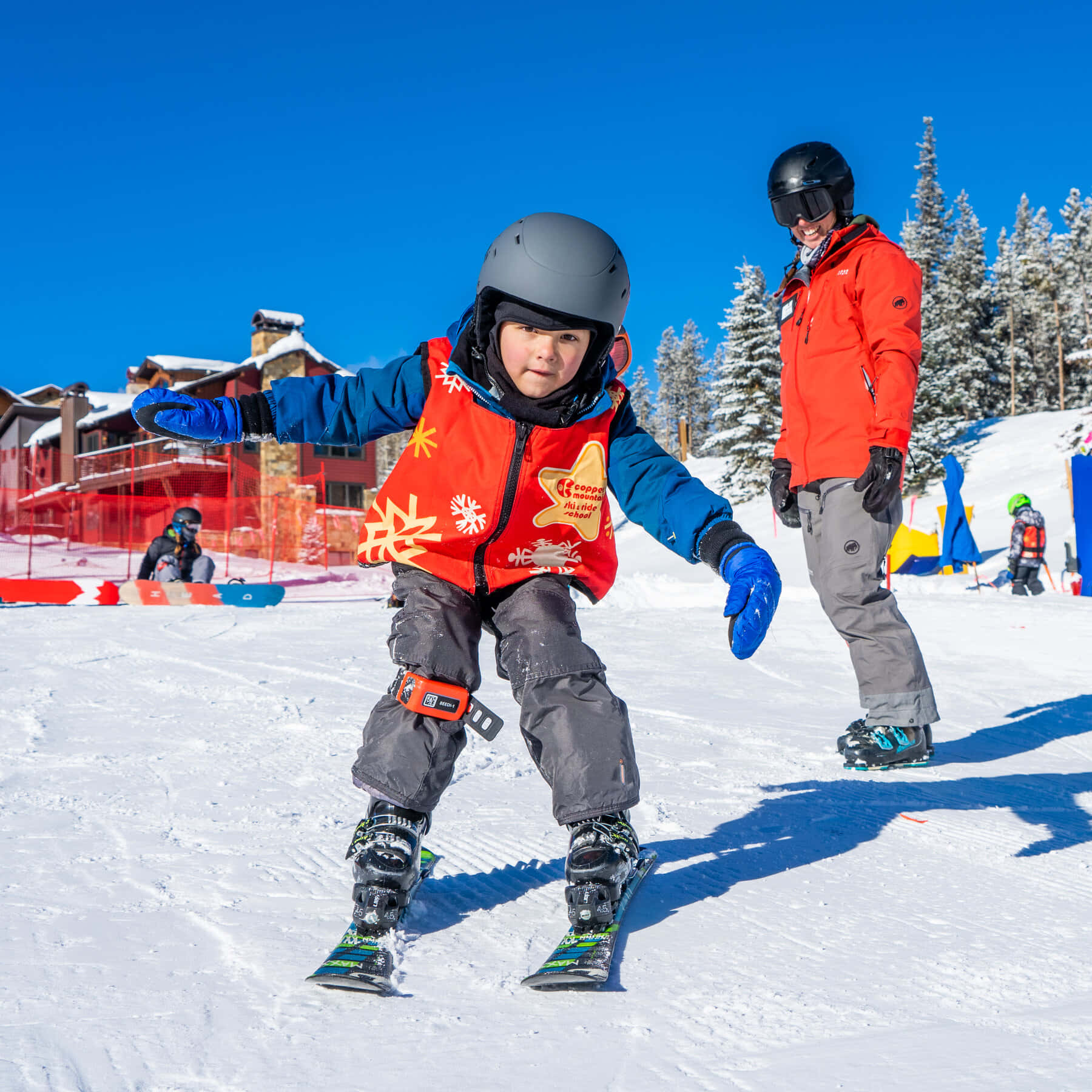 ski 桌布 壁紙 — 一名年輕滑雪者穿著鮮豔裝備，在晴朗藍天下沿著雪坡滑下，附近有成人教練。