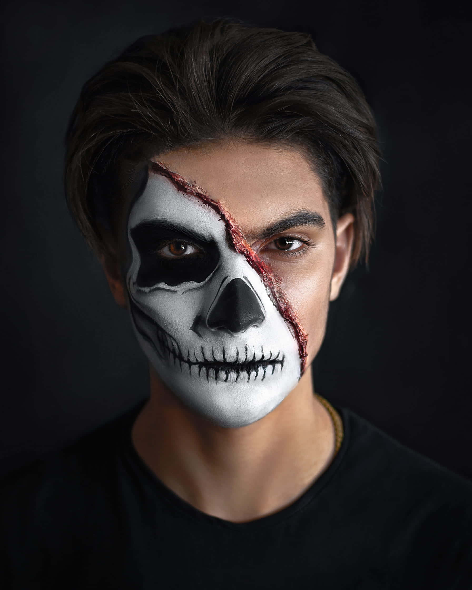 Halloween Face Paint 桌布 壁紙 — 一名年輕男子，半邊臉被畫成骷髏，另一半則展示其自然面貌，背景為深色。